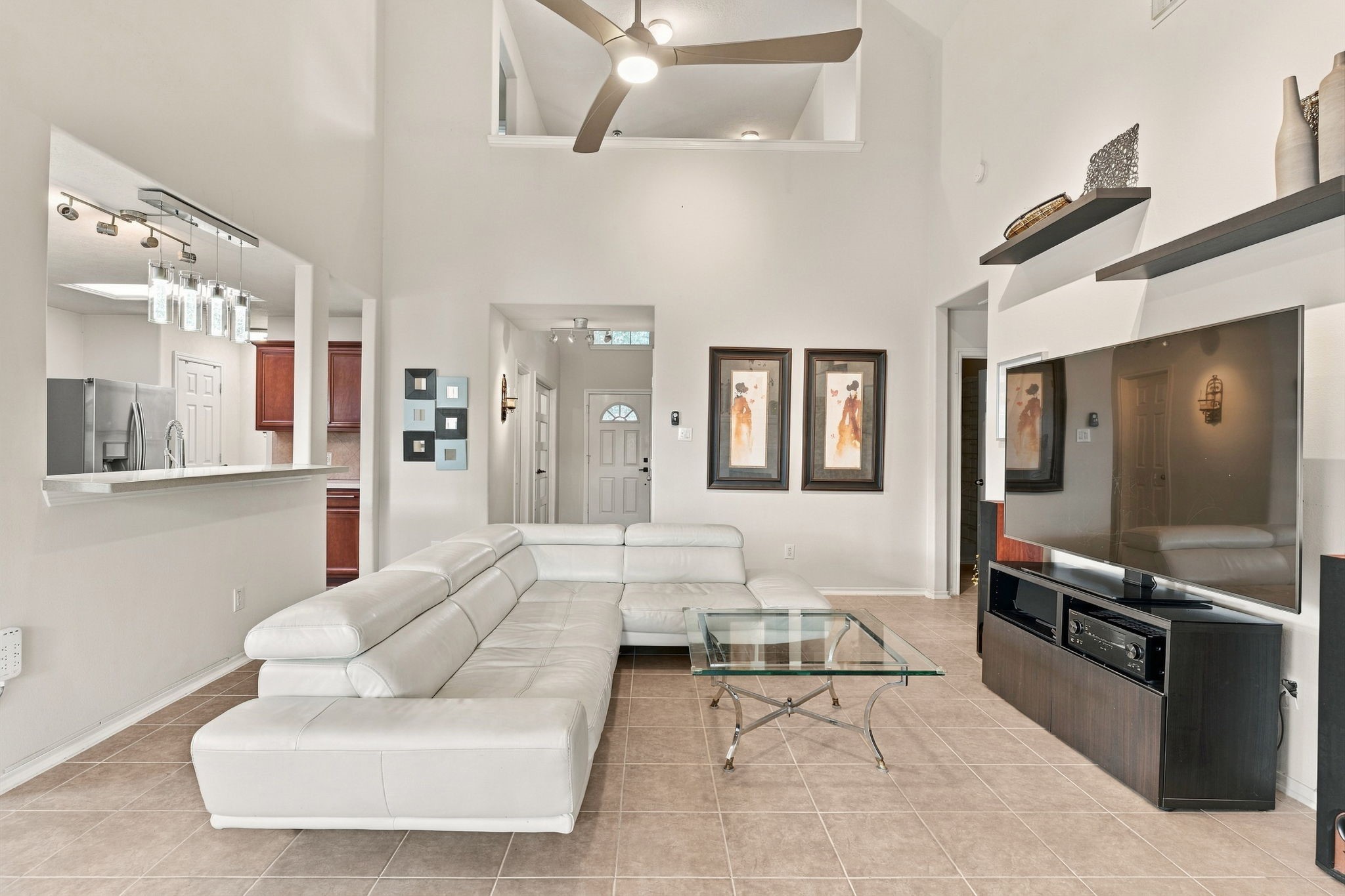 Spacious living area with high ceilings and modern design, featuring a sleek white sectional, large flat-screen TV, and open access to the kitchen, perfect for entertaining.