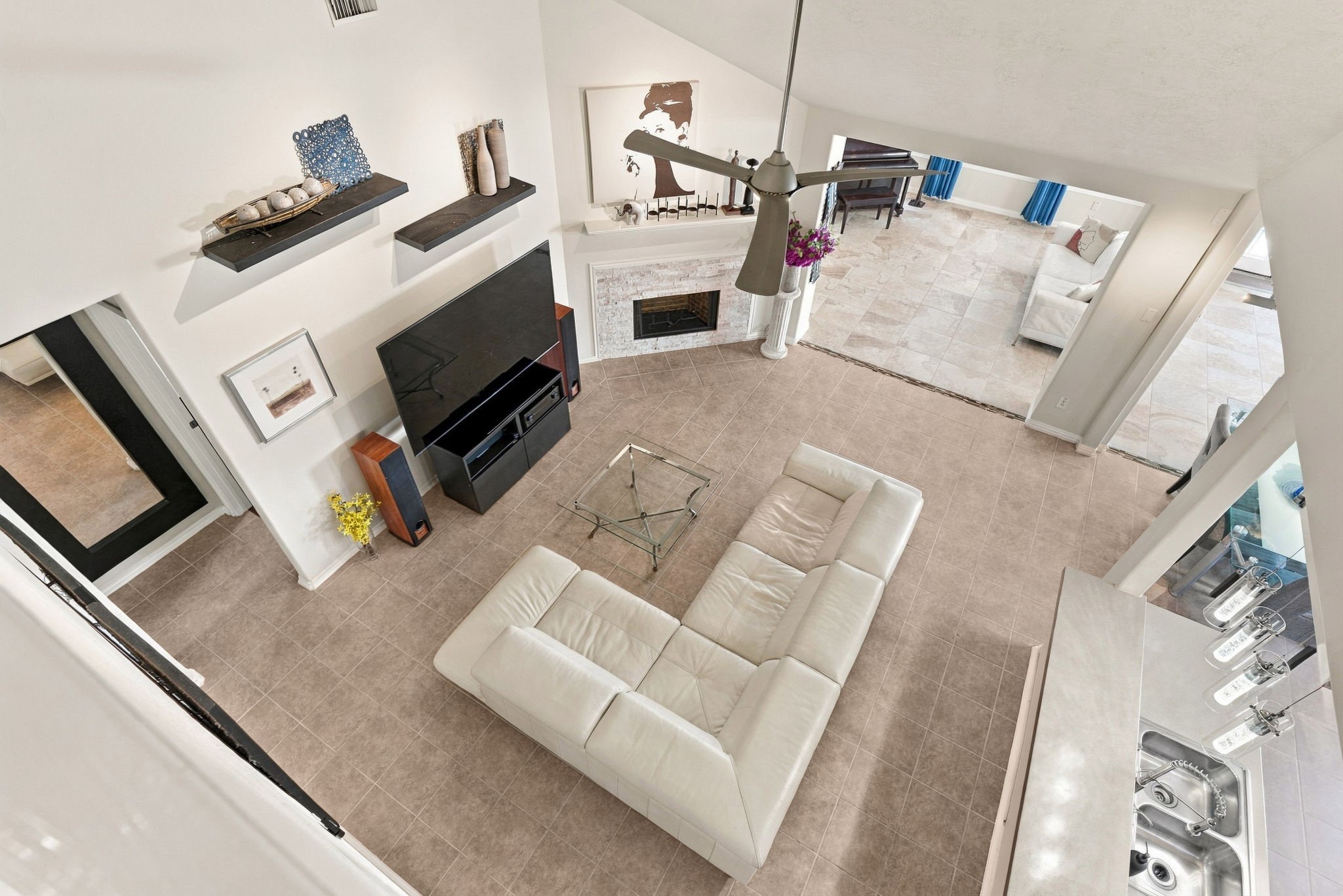 Spacious open-concept living area with high ceilings, a cozy fireplace, and elegant tile flooring. A large sectional sofa faces a modern entertainment center, while a sleek kitchen bar and adjacent dining area provide ample seating and entertainment options. (Furniture not included)