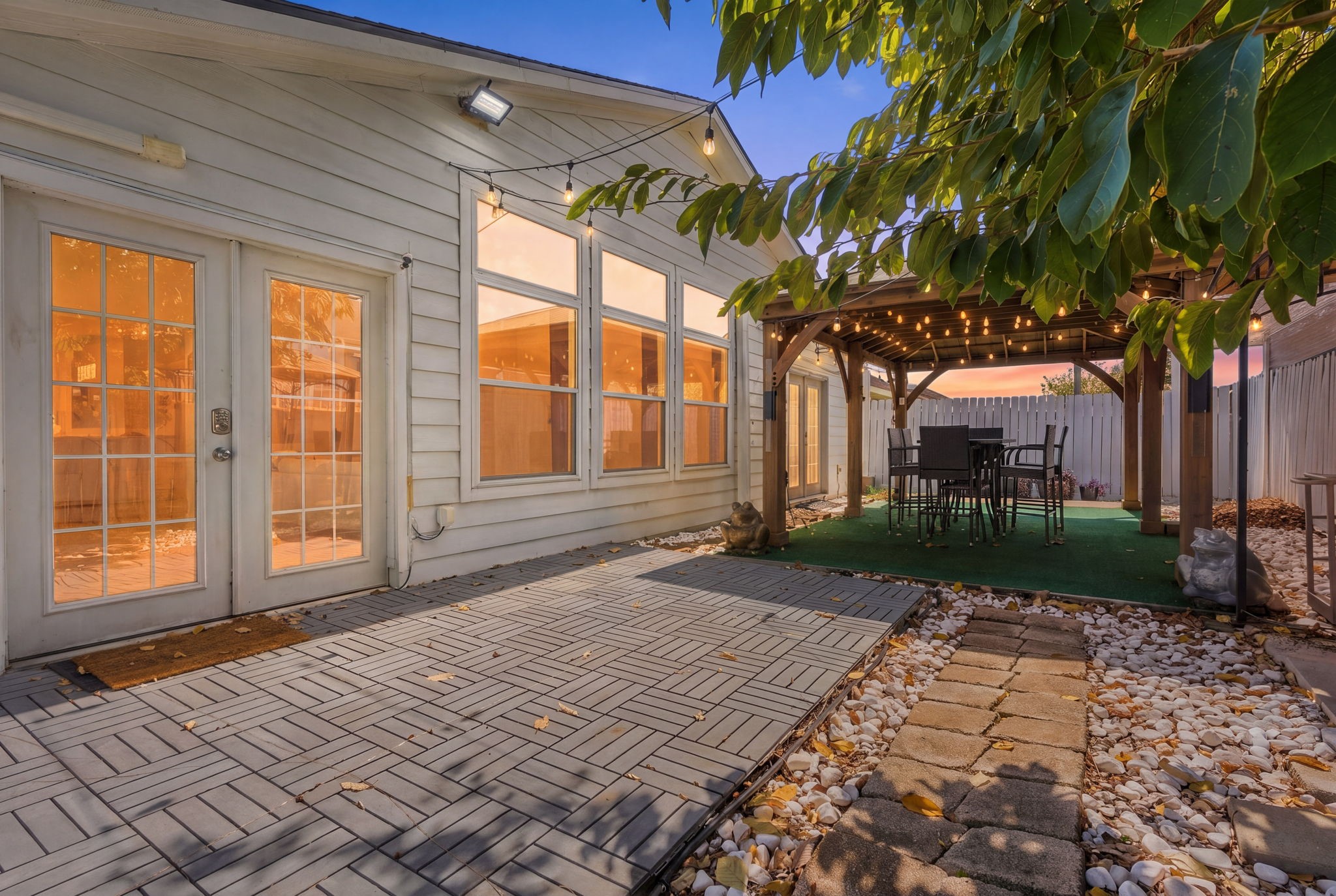 Charming backyard oasis featuring a spacious patio with elegant French doors, a cozy pergola adorned with string lights, and a stylish outdoor dining area, perfect for entertaining.