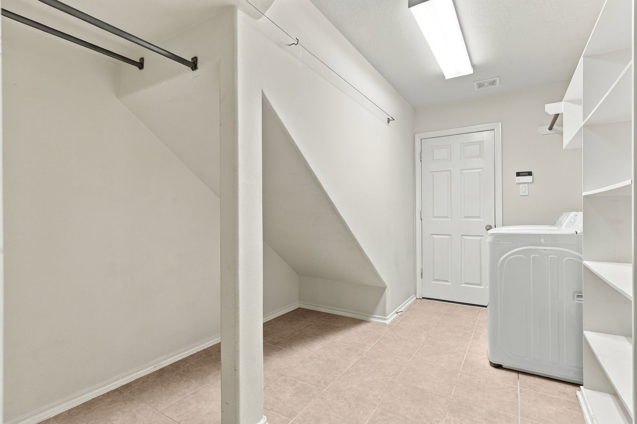 Spacious laundry room with ample shelving and storage, featuring a washing machine and convenient access to the adjacent area.