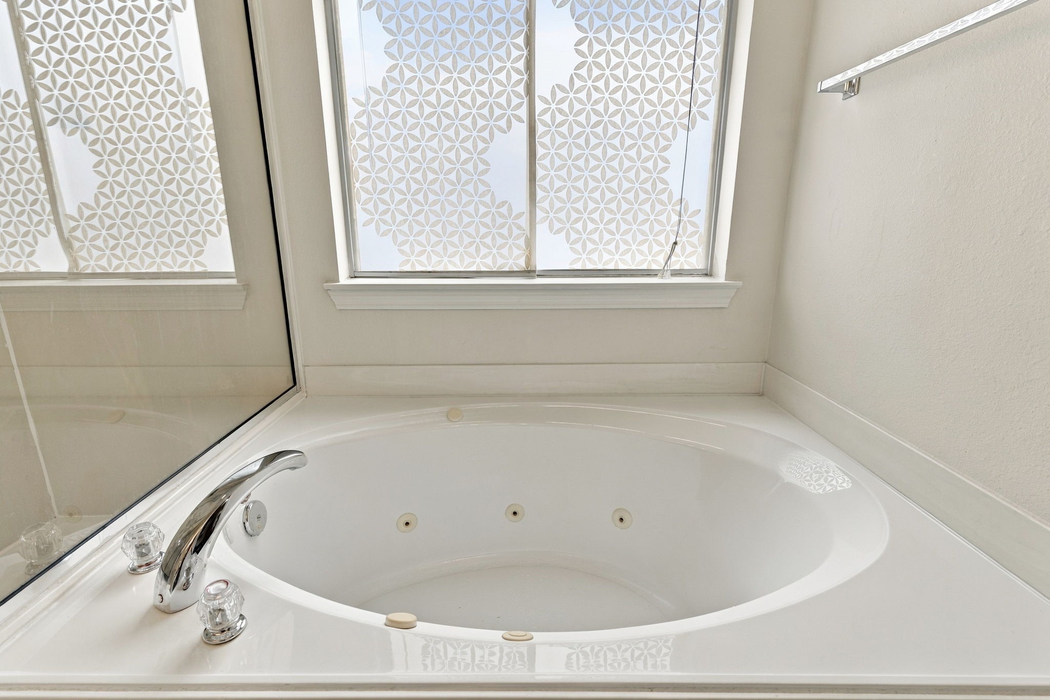 Luxurious Jacuzzi tub with elegant fixtures, complemented by a beautifully patterned privacy window for a serene bathing experience.