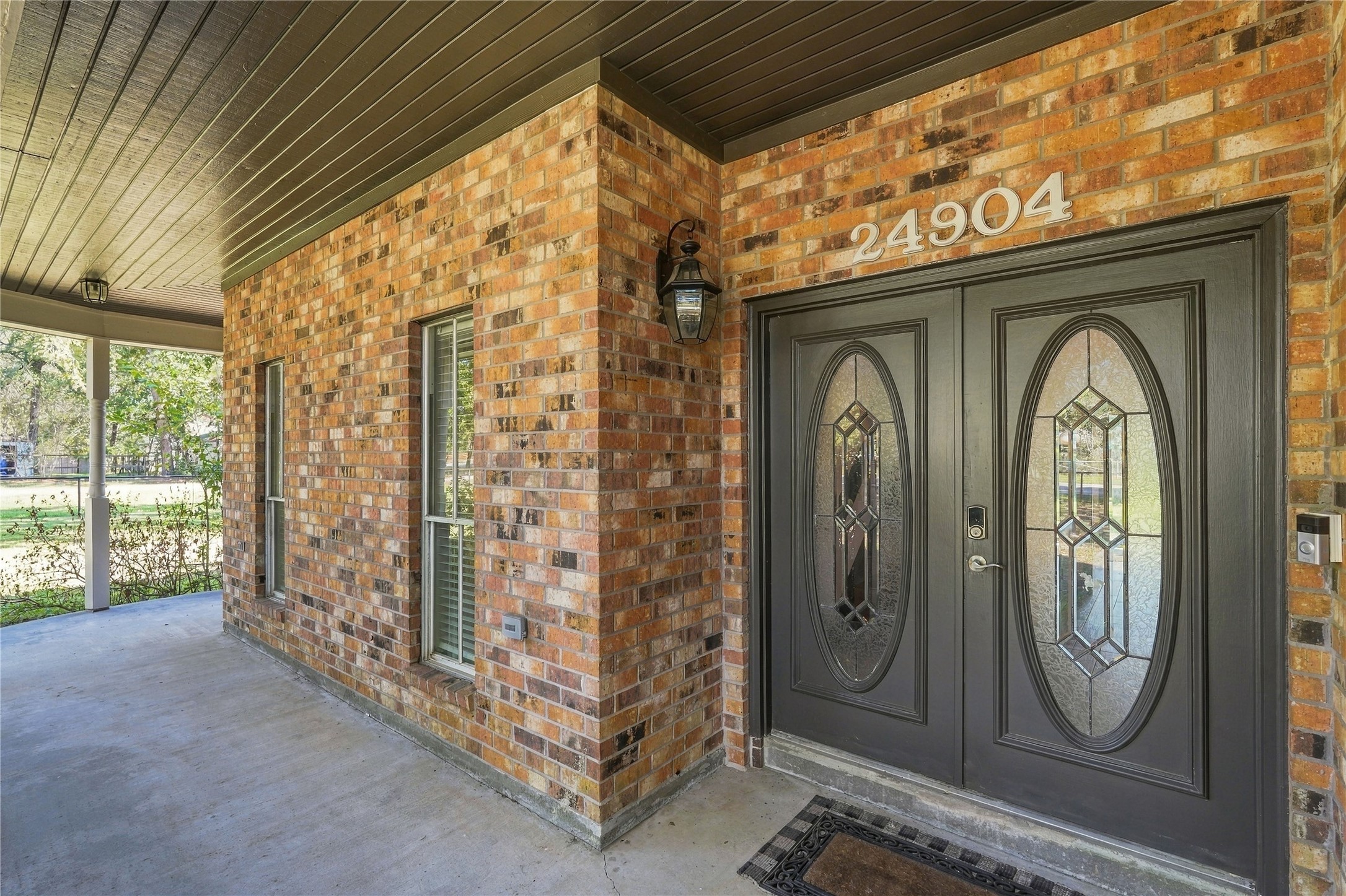 Welcoming covered front porch with decorative glass double entry doors and classic brick exterior.