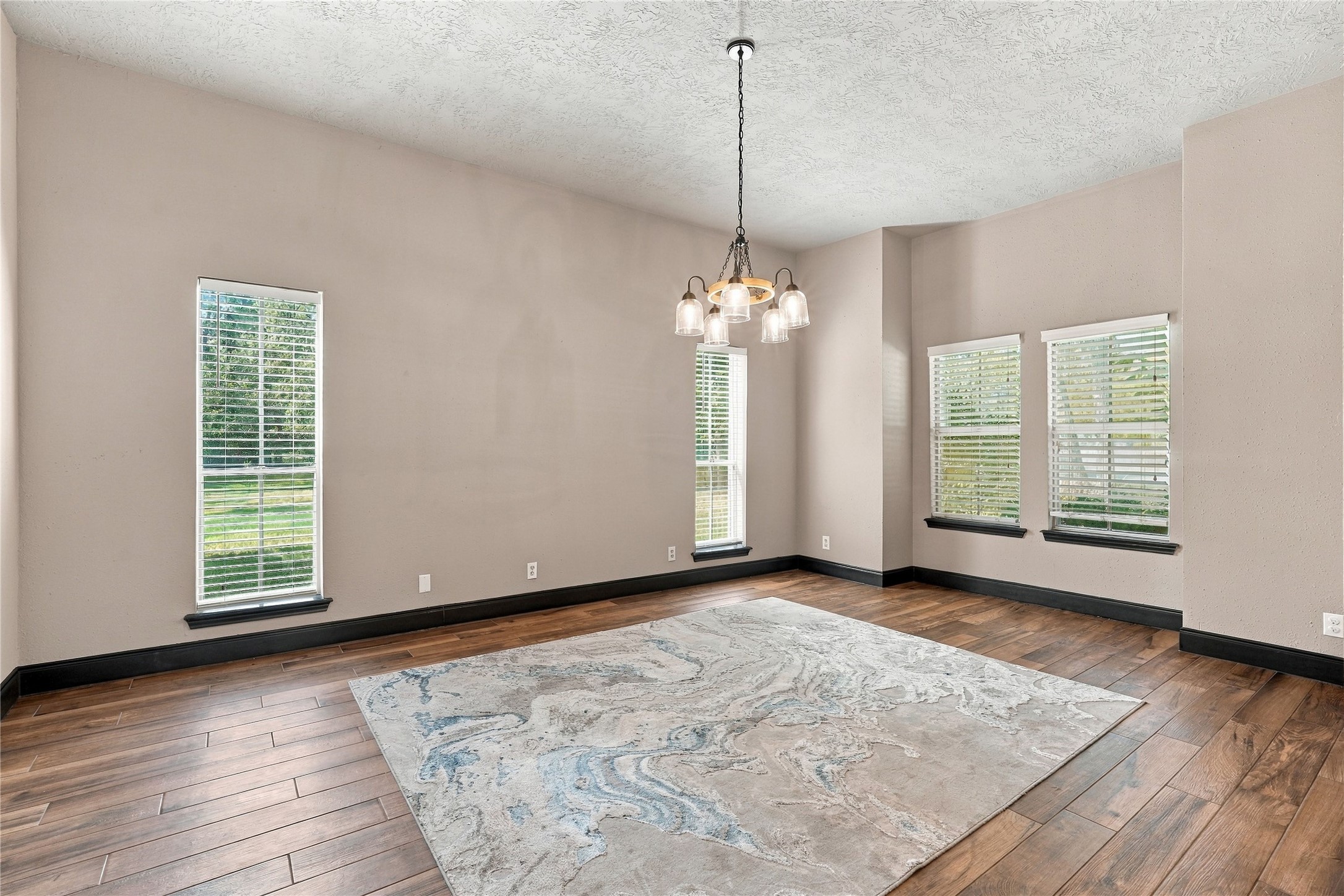 Spacious formal dining room with wood-look flooring, high ceilings, decorative chandelier, and multiple windows providing natural light.