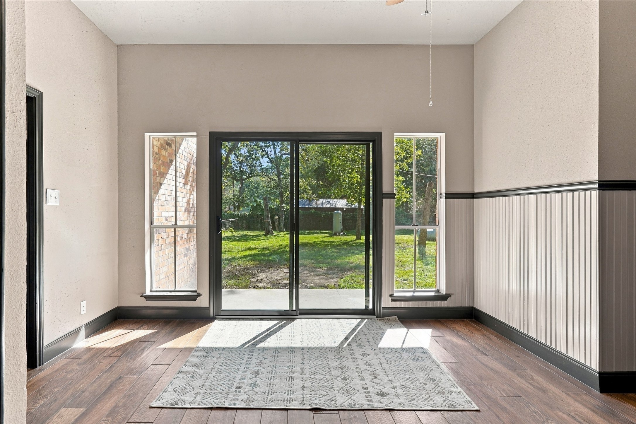 Light-filled breakfast room with new sliding glass doors leading to the backyard patio, large windows, and decorative wainscoting.