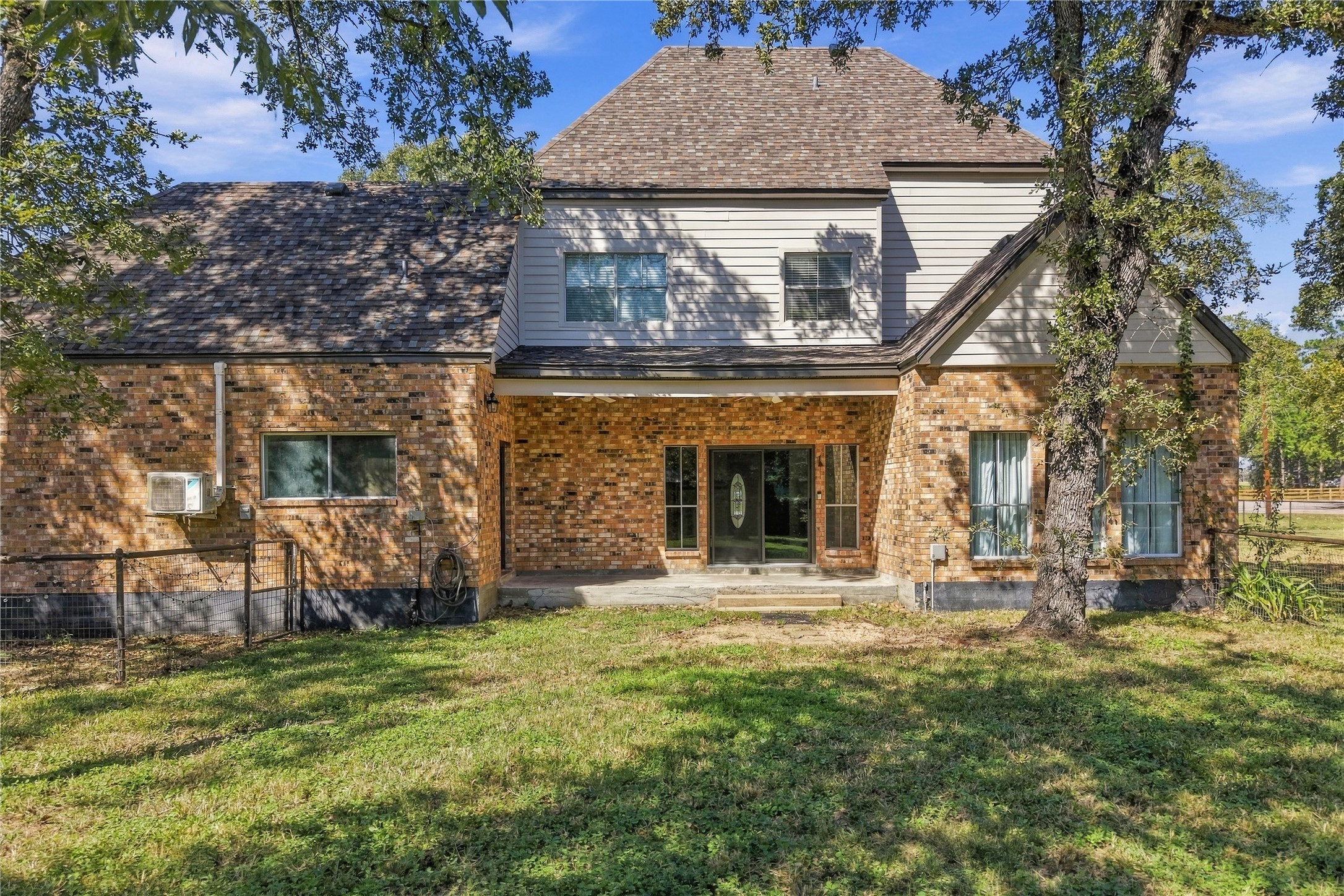 Rear exterior featuring a covered patio, brick exterior, and views of the tree-shaded backyard.