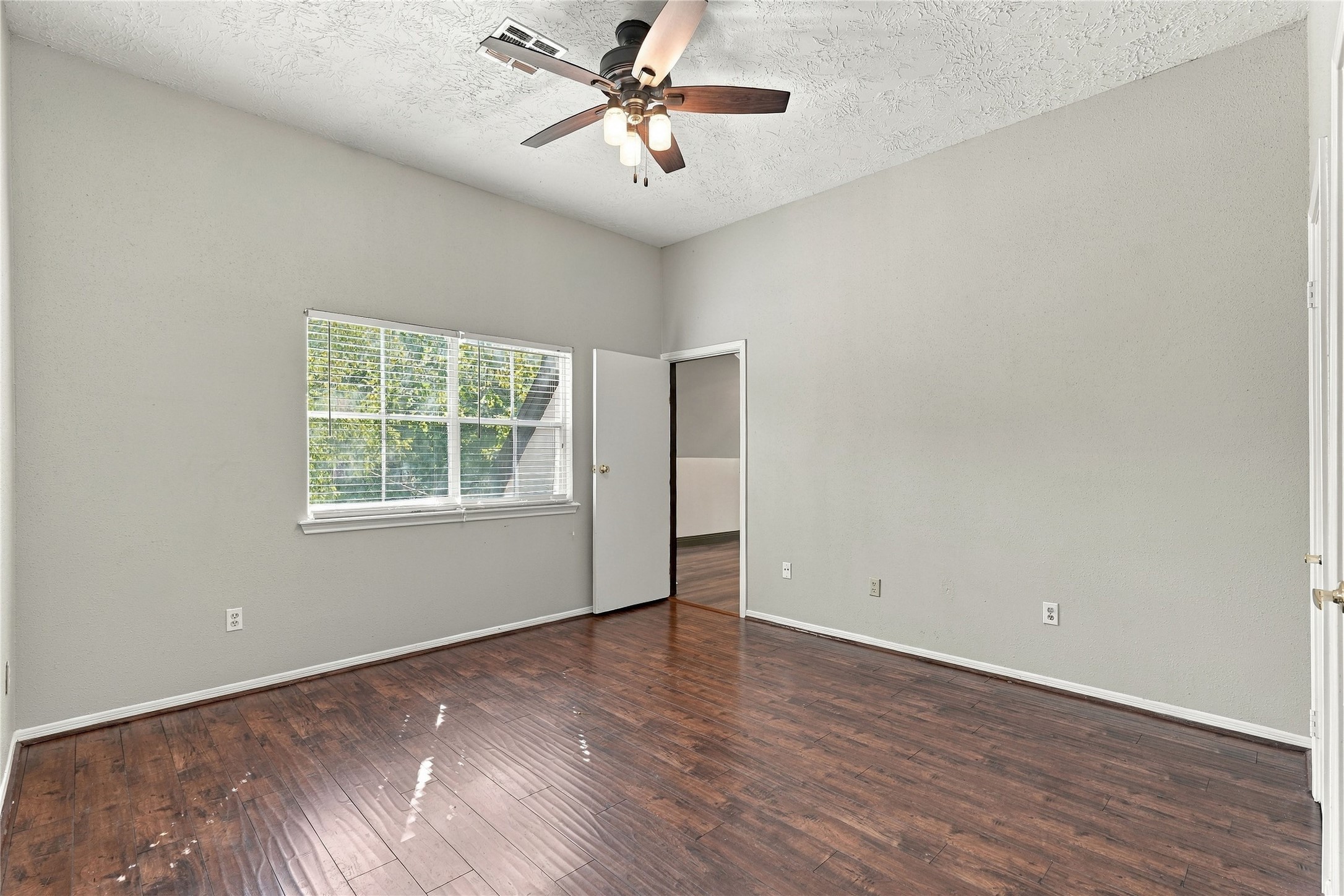 Upstairs secondary bedroom with wood flooring, ceiling fan, and a large window offering views of the mature trees.