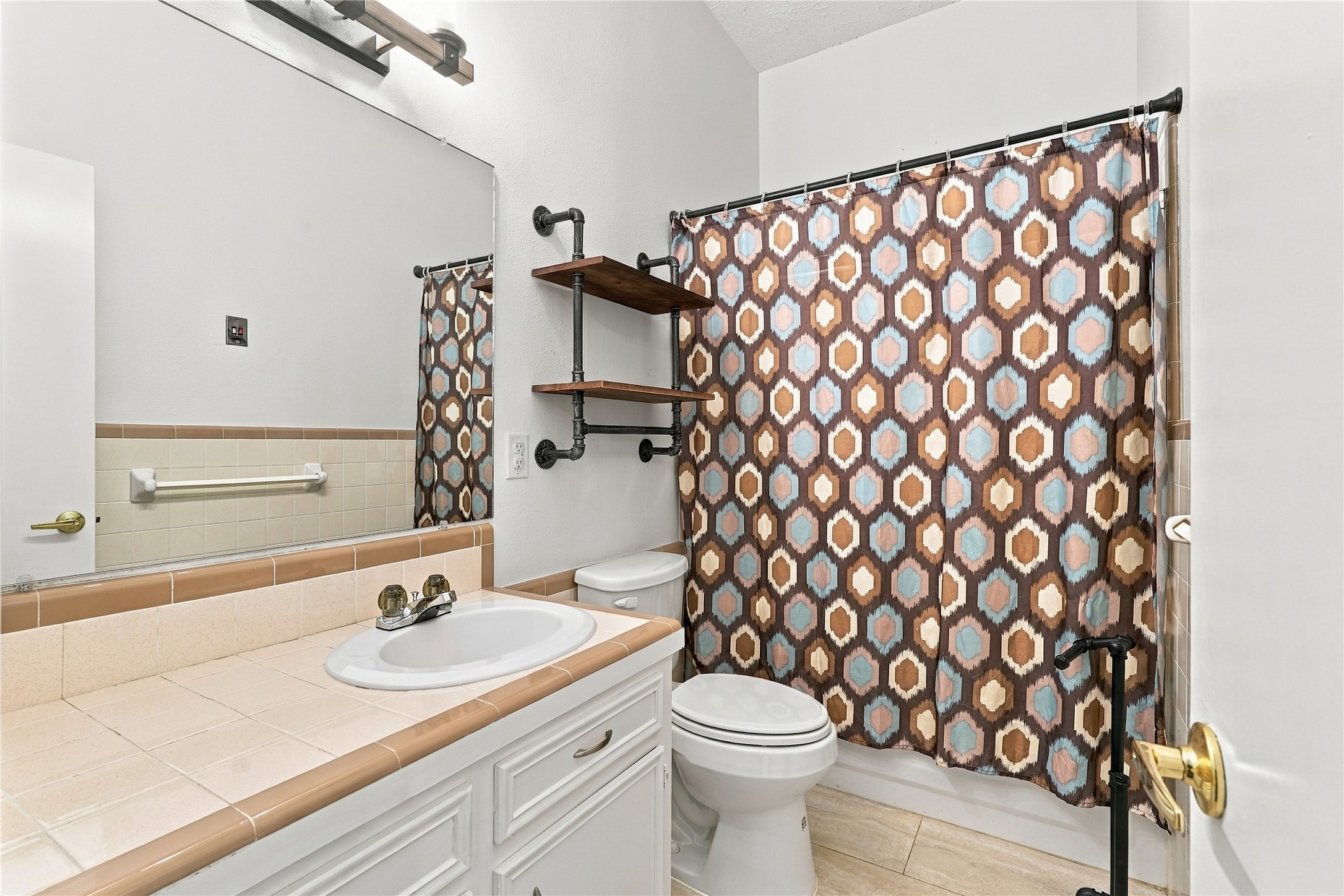 Upstairs secondary bathroom featuring a tub/shower combination, tile countertop, vanity storage, and additional wall shelving.