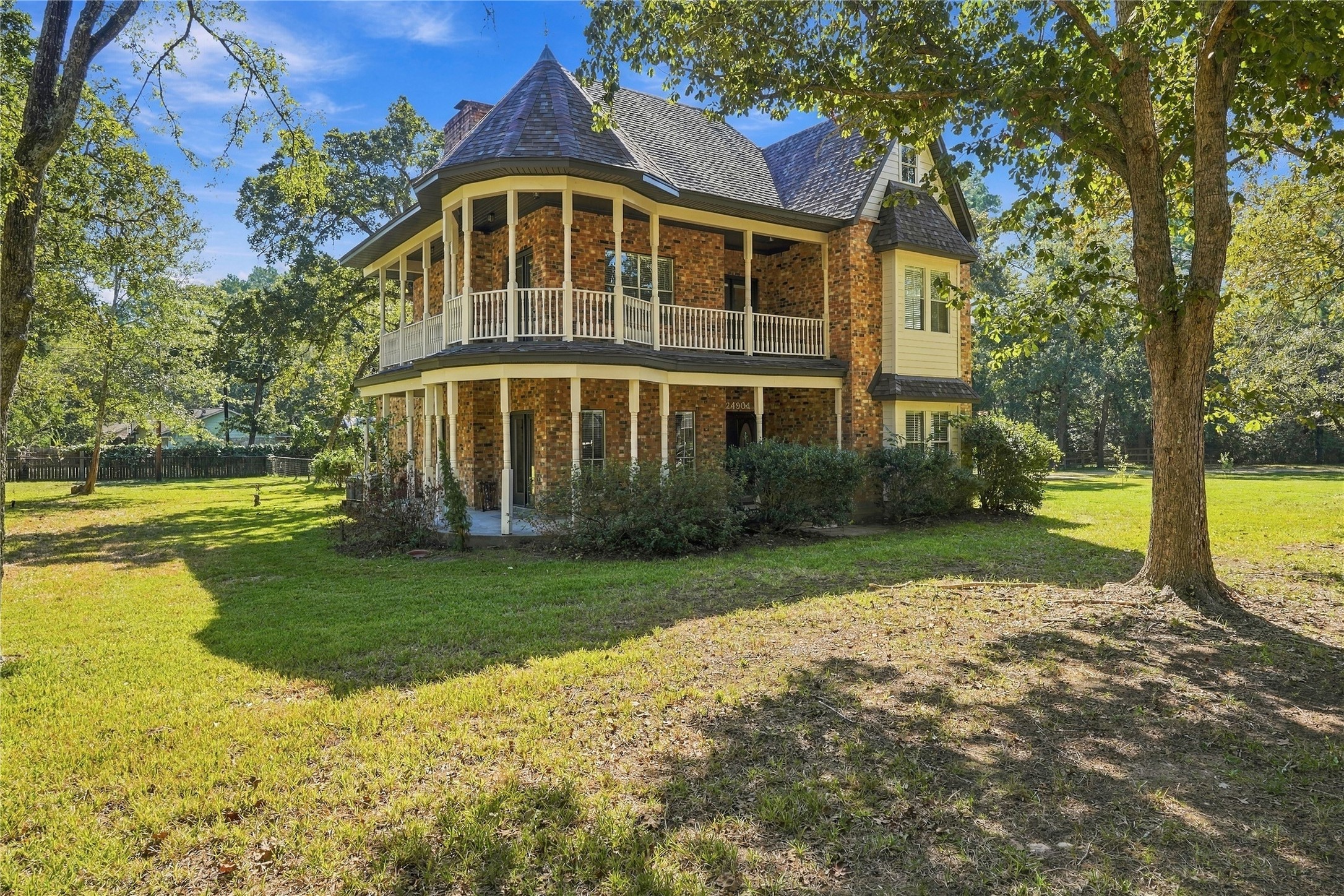 Additional exterior view showcasing the distinctive architecture, wraparound covered porch, upper balcony, and spacious tree-lined yard.
