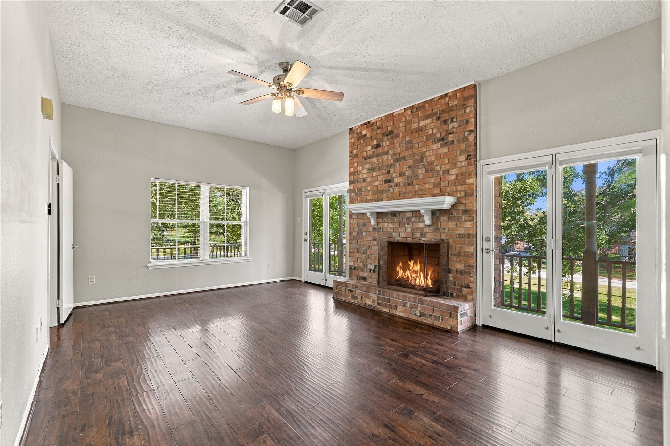 Additional view of the primary bedroom highlighting the brick fireplace, generous floor space, and multiple windows and French doors overlooking the property.