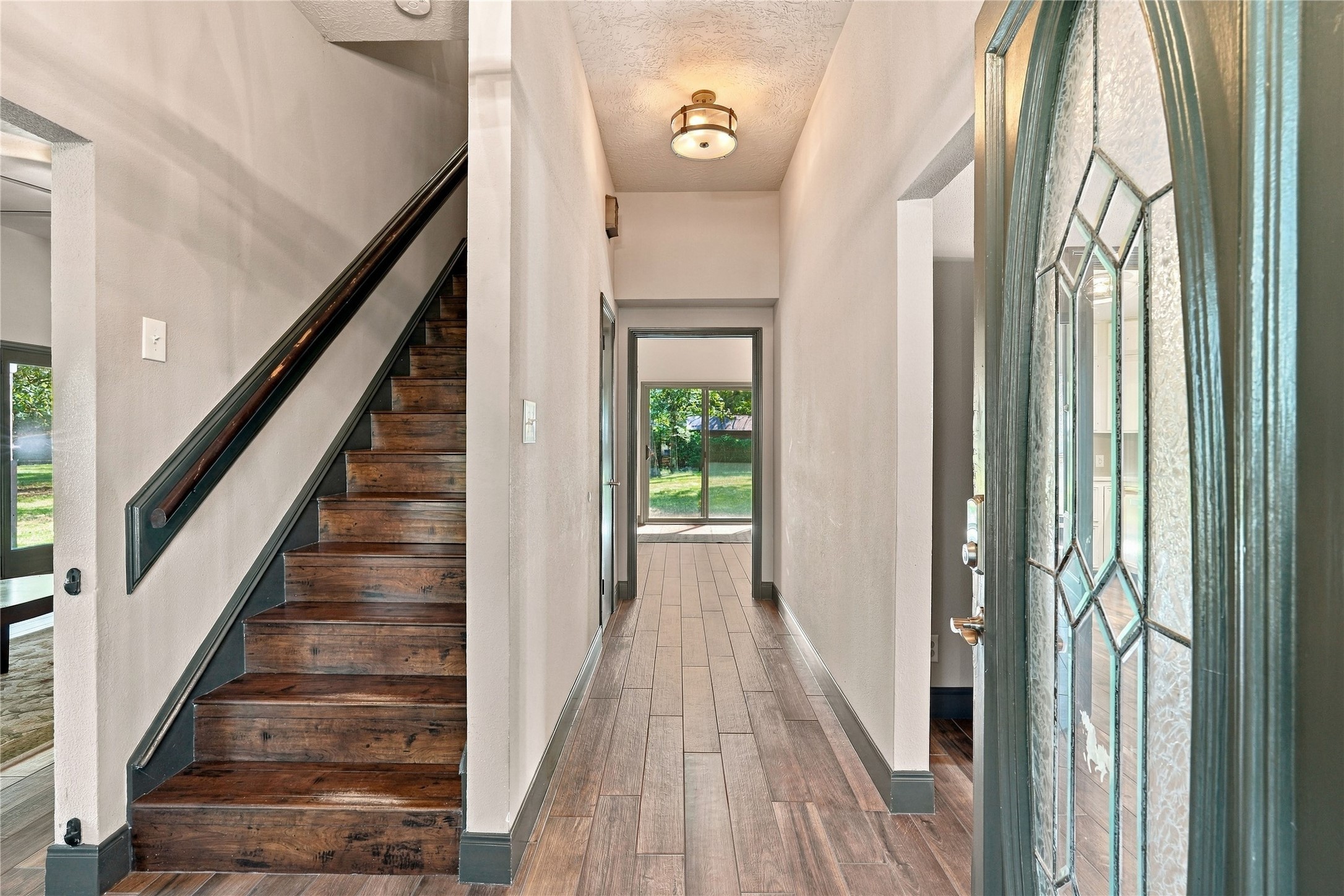 Inviting entryway featuring wood-look flooring, staircase with wood treads, and views toward the rear of the home.