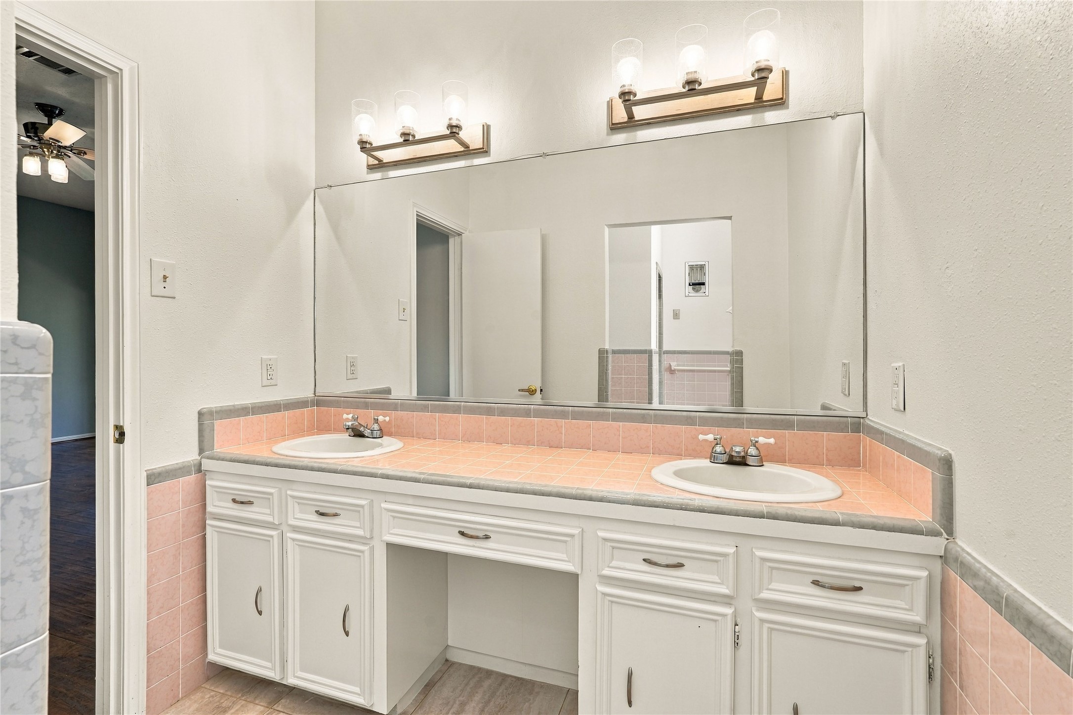 Primary bathroom featuring double sinks, an extended tile countertop, large vanity mirror, and ample cabinet storage.