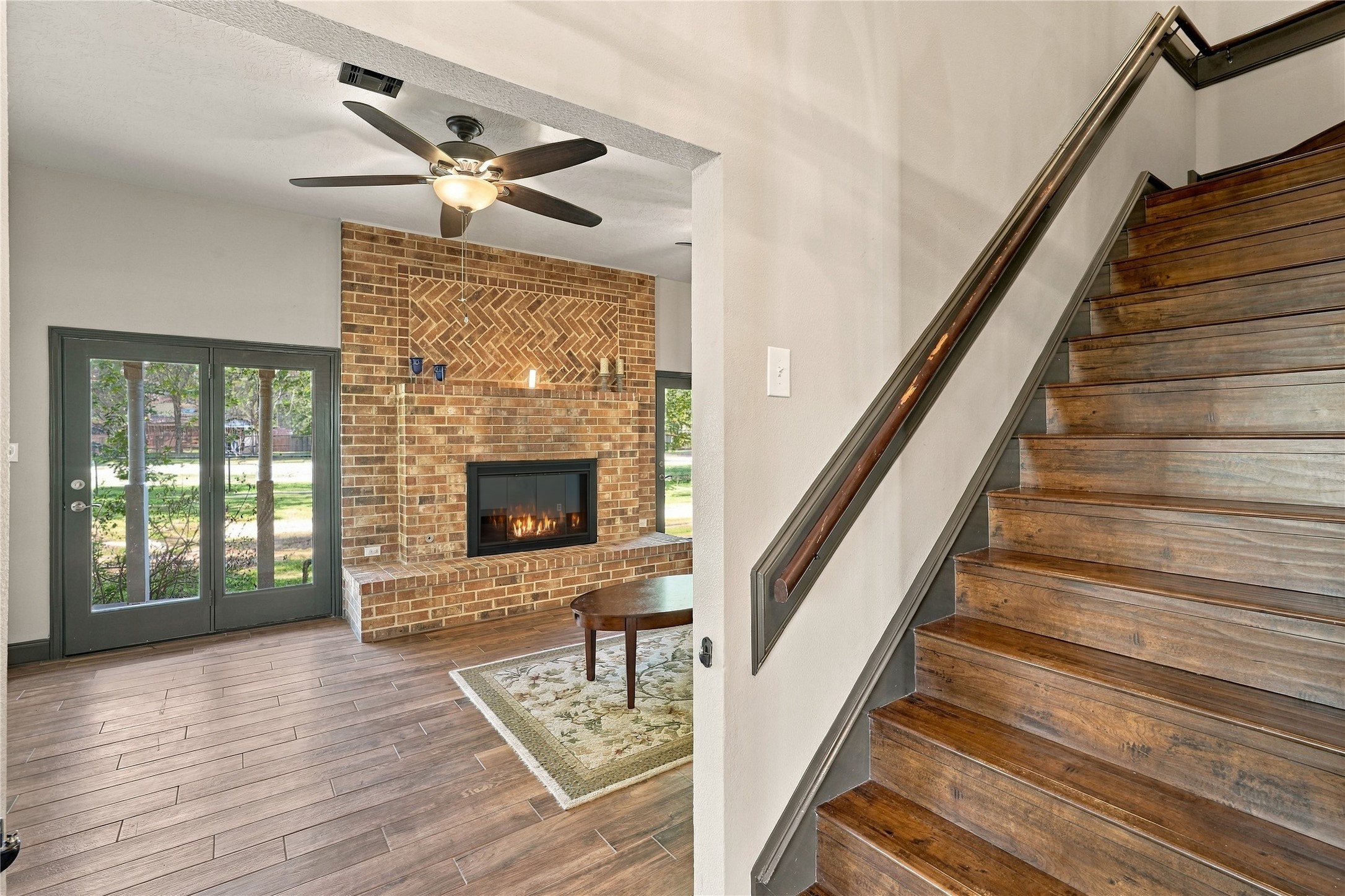 View from the entry showcasing the living room's floor-to-ceiling brick fireplace, wood-look flooring, and staircase.