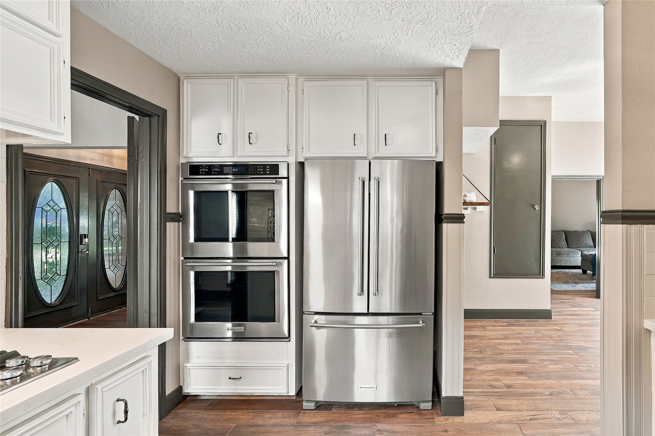 Stainless steel double ovens and French-door refrigerator surrounded by white cabinetry, with convenient access to the adjoining living areas.