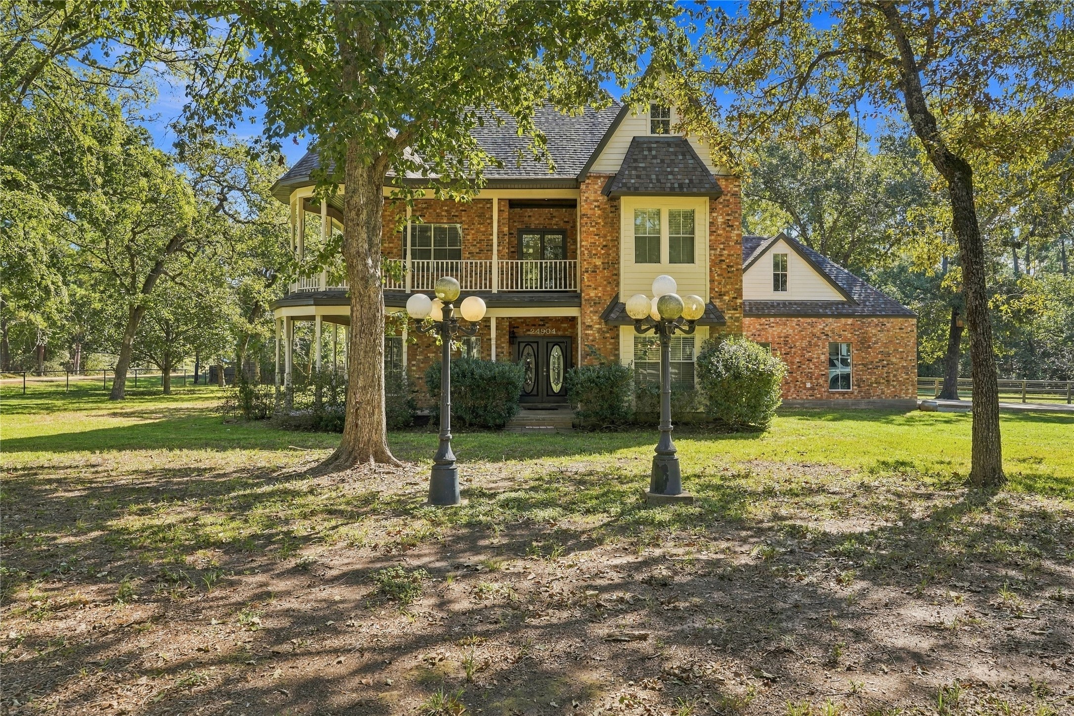 Beautiful two-story brick home surrounded by mature trees, featuring a covered front porch and second-story balcony.