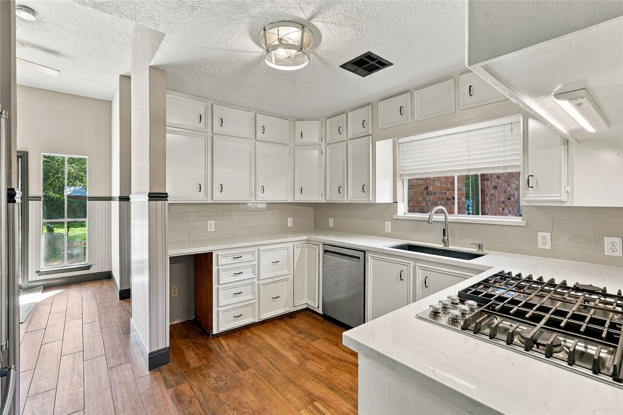 Bright kitchen featuring white cabinetry, quartz countertops, subway tile backsplash, stainless steel appliances, and wood flooring.