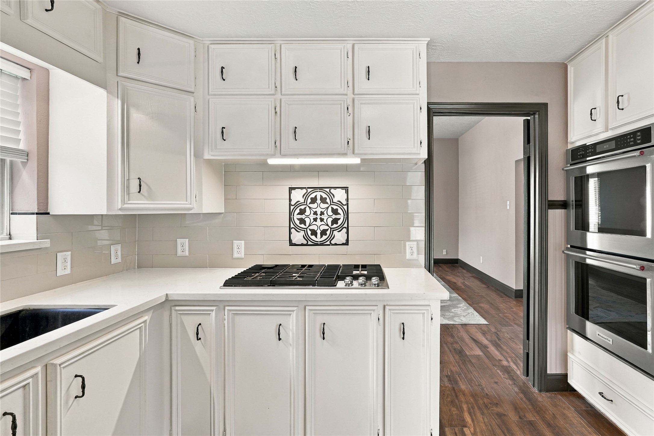 Kitchen featuring a built-in gas cooktop, decorative tile backsplash accent, white cabinetry, and double wall ovens.