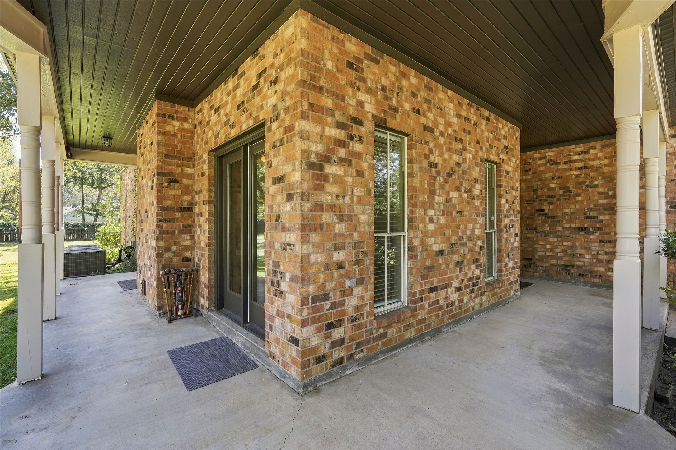 Covered ground-level patio with concrete flooring, brick exterior, and access to the surrounding yard.
