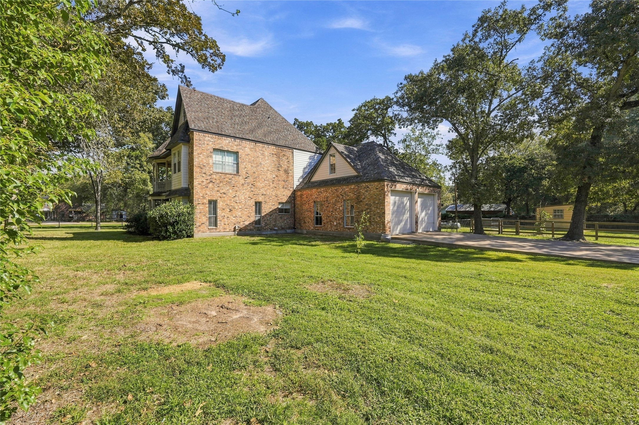 Side exterior showcasing the brick home, attached two-car garage, and spacious lawn surrounded by mature trees.