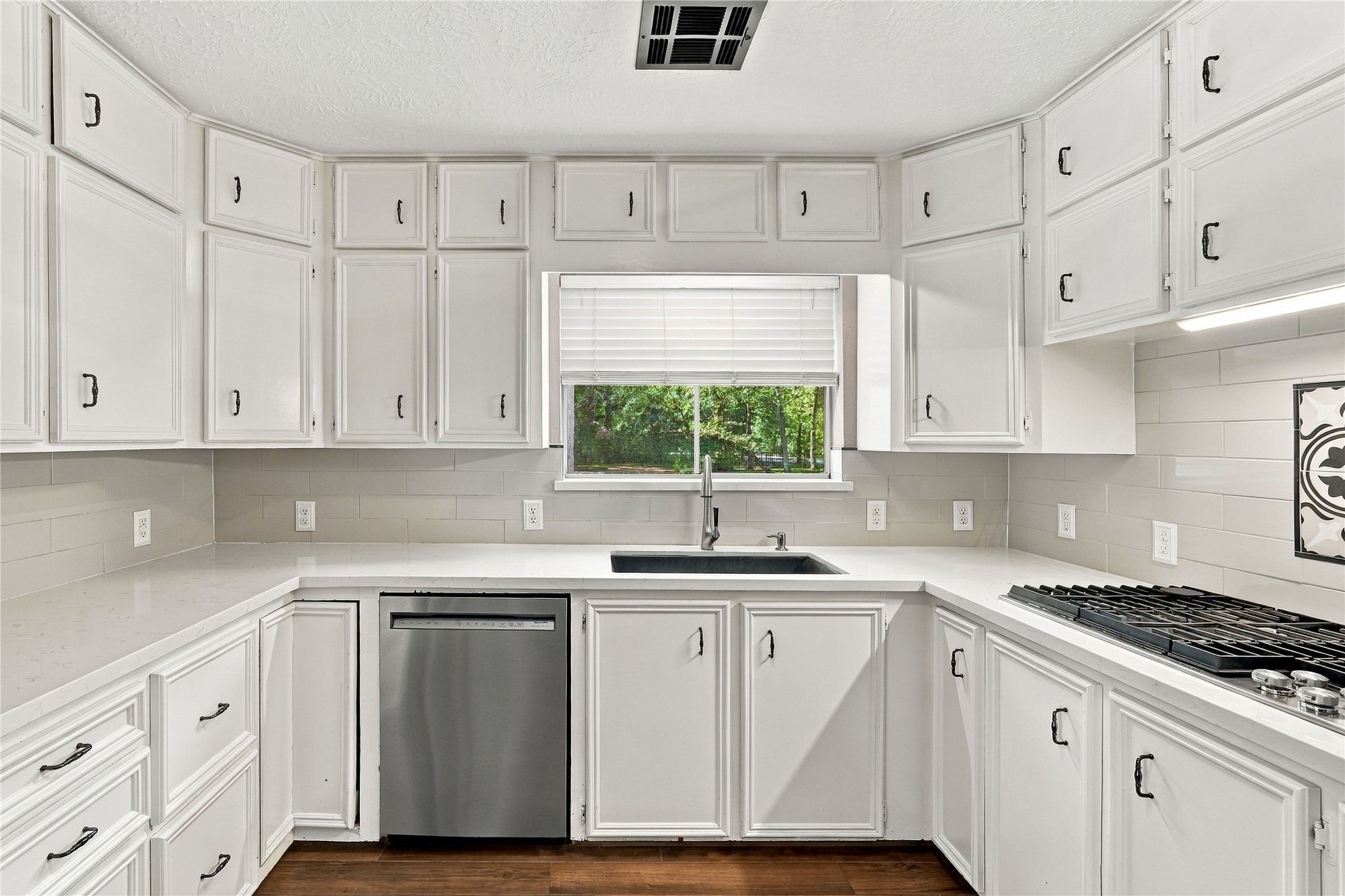 Additional kitchen view highlighting abundant cabinet storage, generous counter space, stainless steel dishwasher, and window overlooking the backyard.