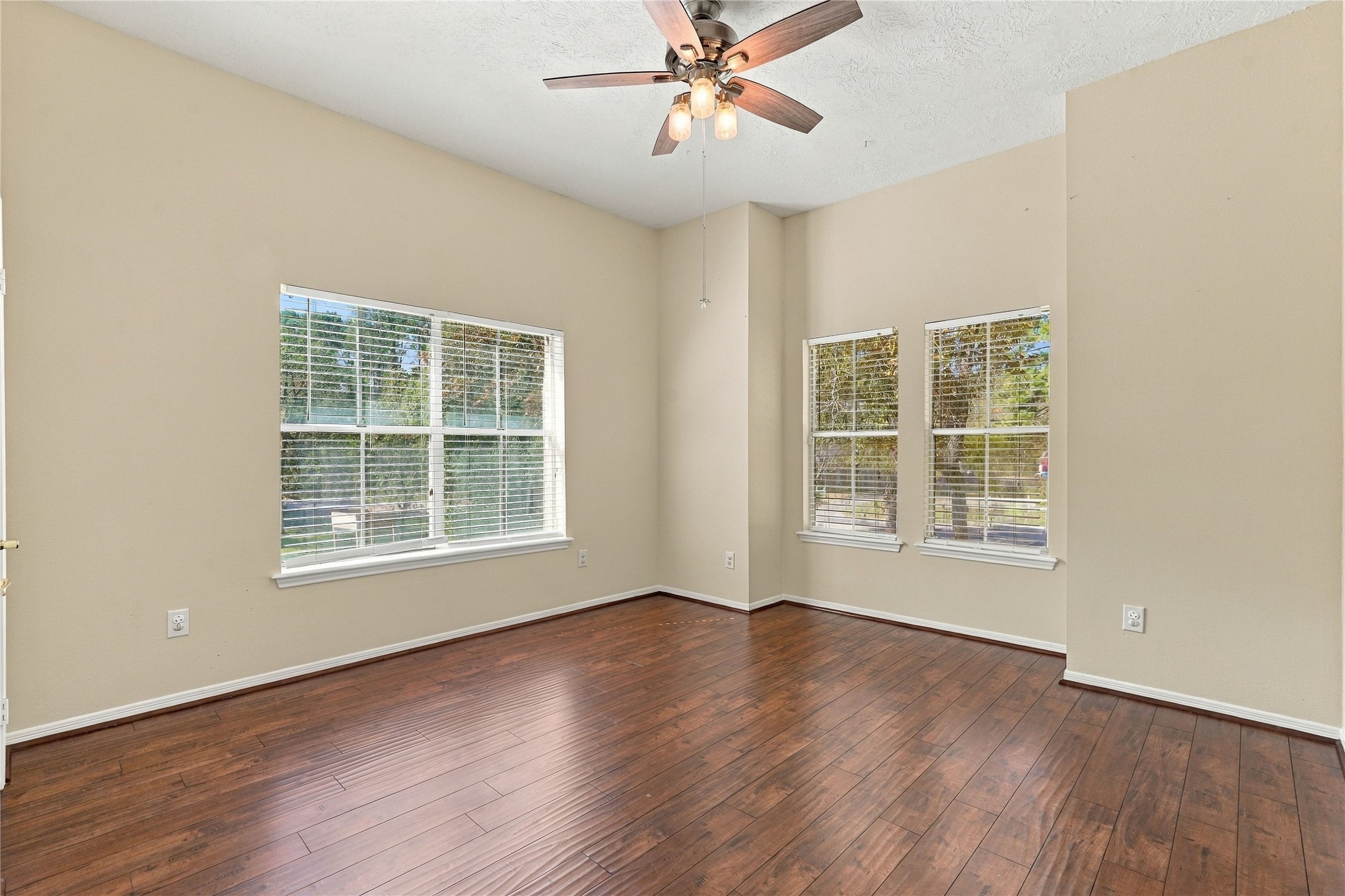 Spacious upstairs secondary bedroom with wood flooring, high ceiling, ceiling fan, and multiple windows overlooking the property.