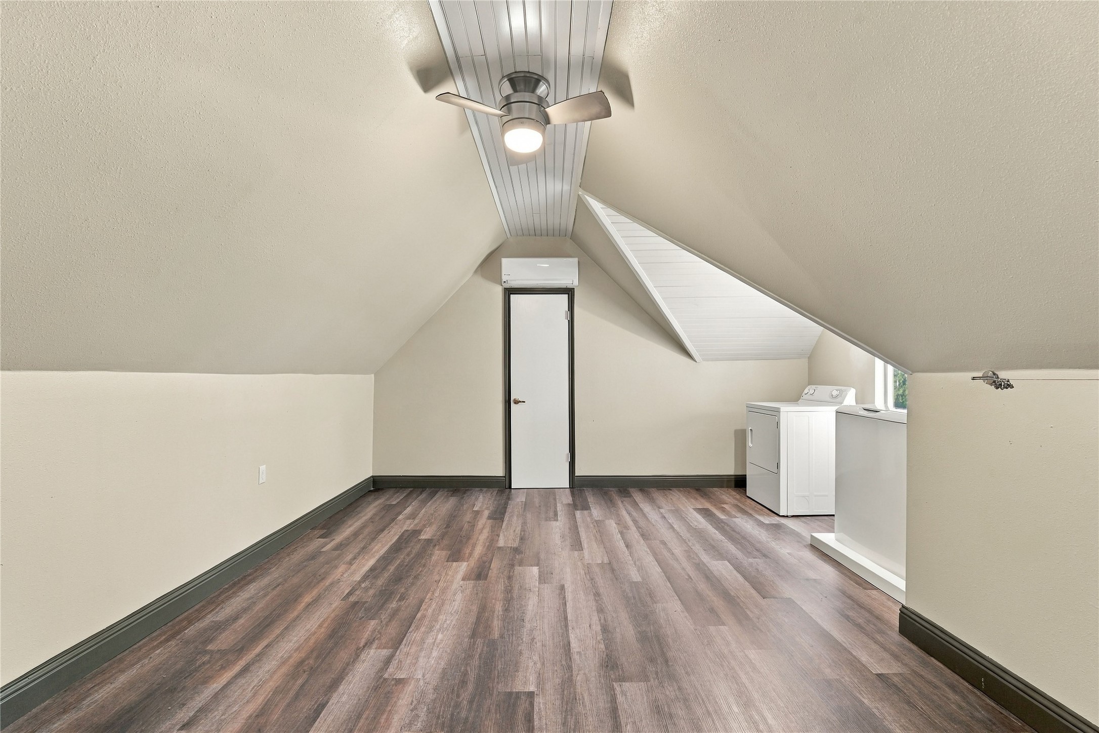 Spacious second-floor laundry and bonus room above the garage, featuring wood-look flooring, vaulted ceilings, and ceiling fan.