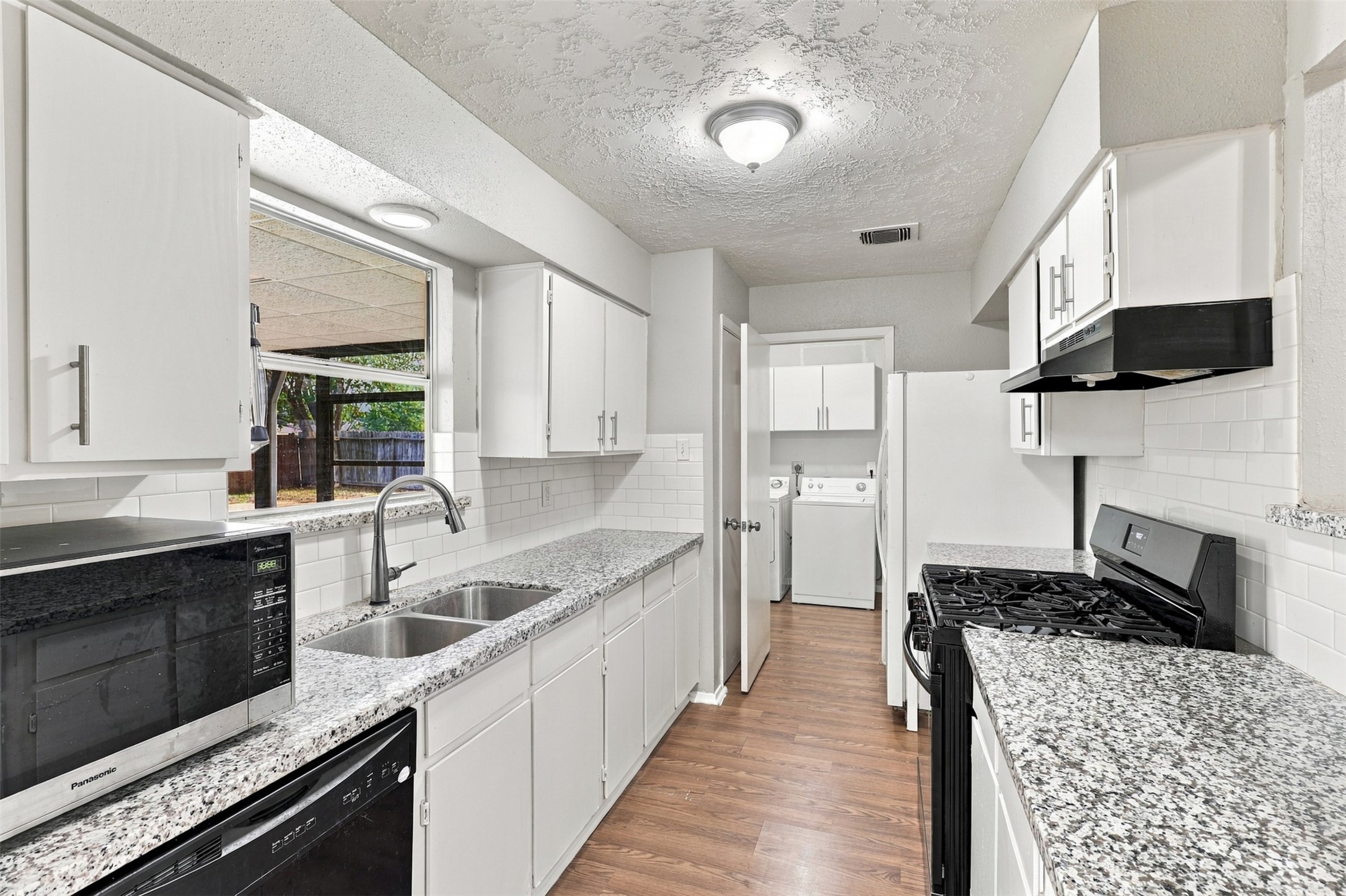 Kitchen features granite countertops, white cabinetry, and a window above the sink for natural light.