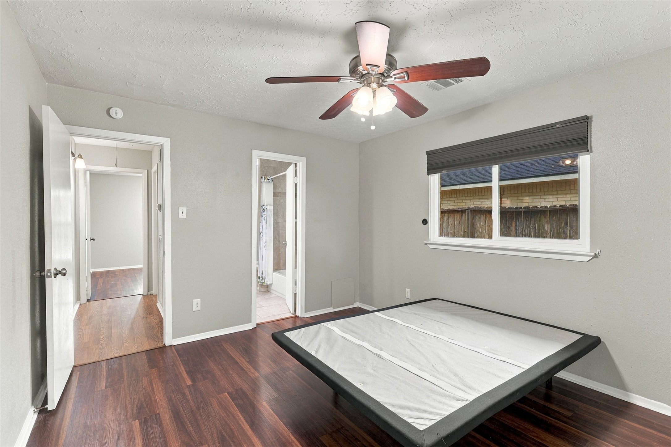 Another primary bedroom view highlights the layout, ceiling fan, and wood-look flooring.