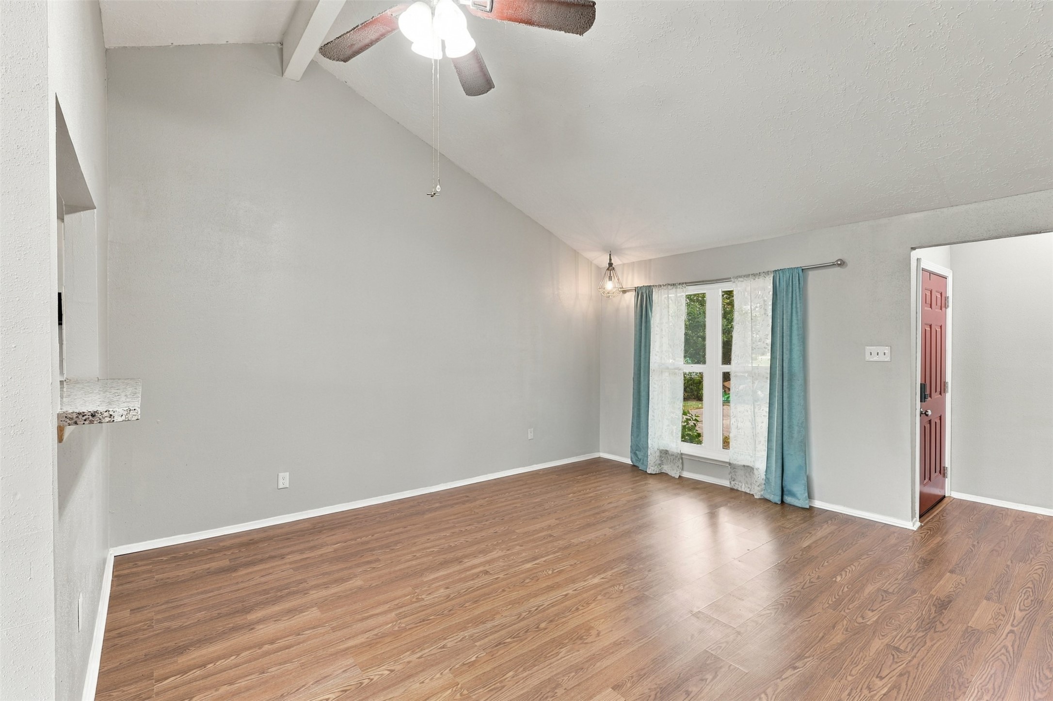 Another view of the living room highlights the high ceiling, wood-look flooring, and front windos.