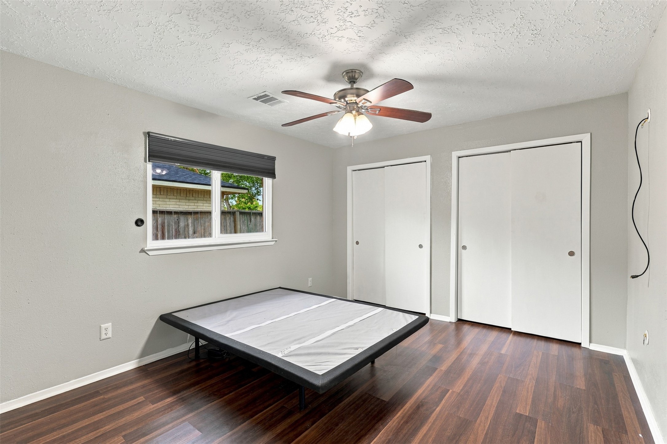 Primary bedroom features wood-look flooring, a ceiling fan, natural light, and double closet doors.