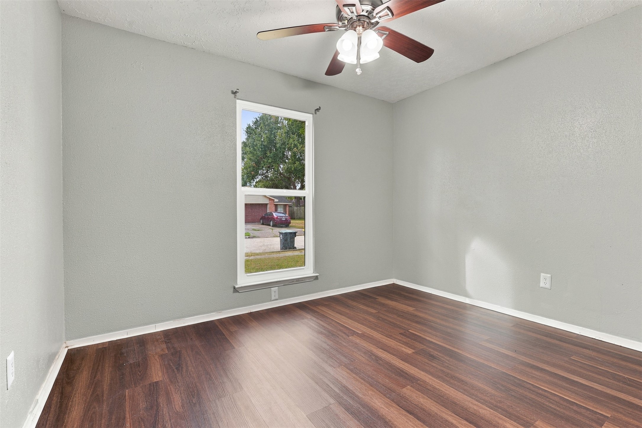 Second bedroom offers a ceiling fan, wood-look flooring, and a window overlooking the outdoors.