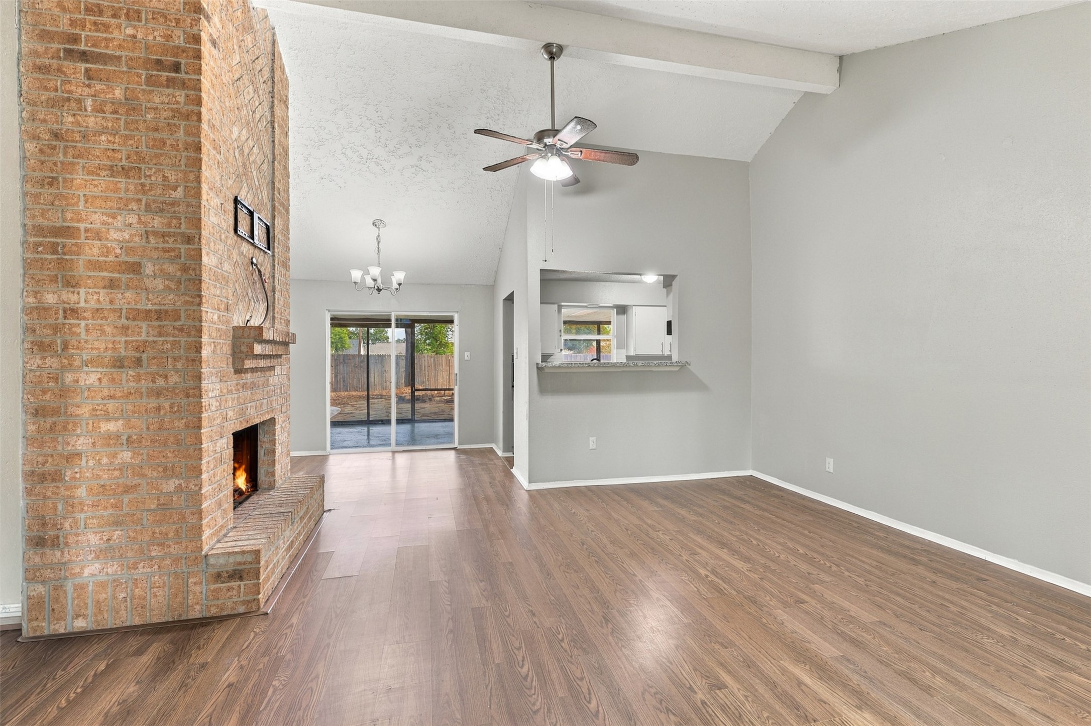 Living room features wood-look flooring, a vaulted ceiling, and an open connection to the kitchen.