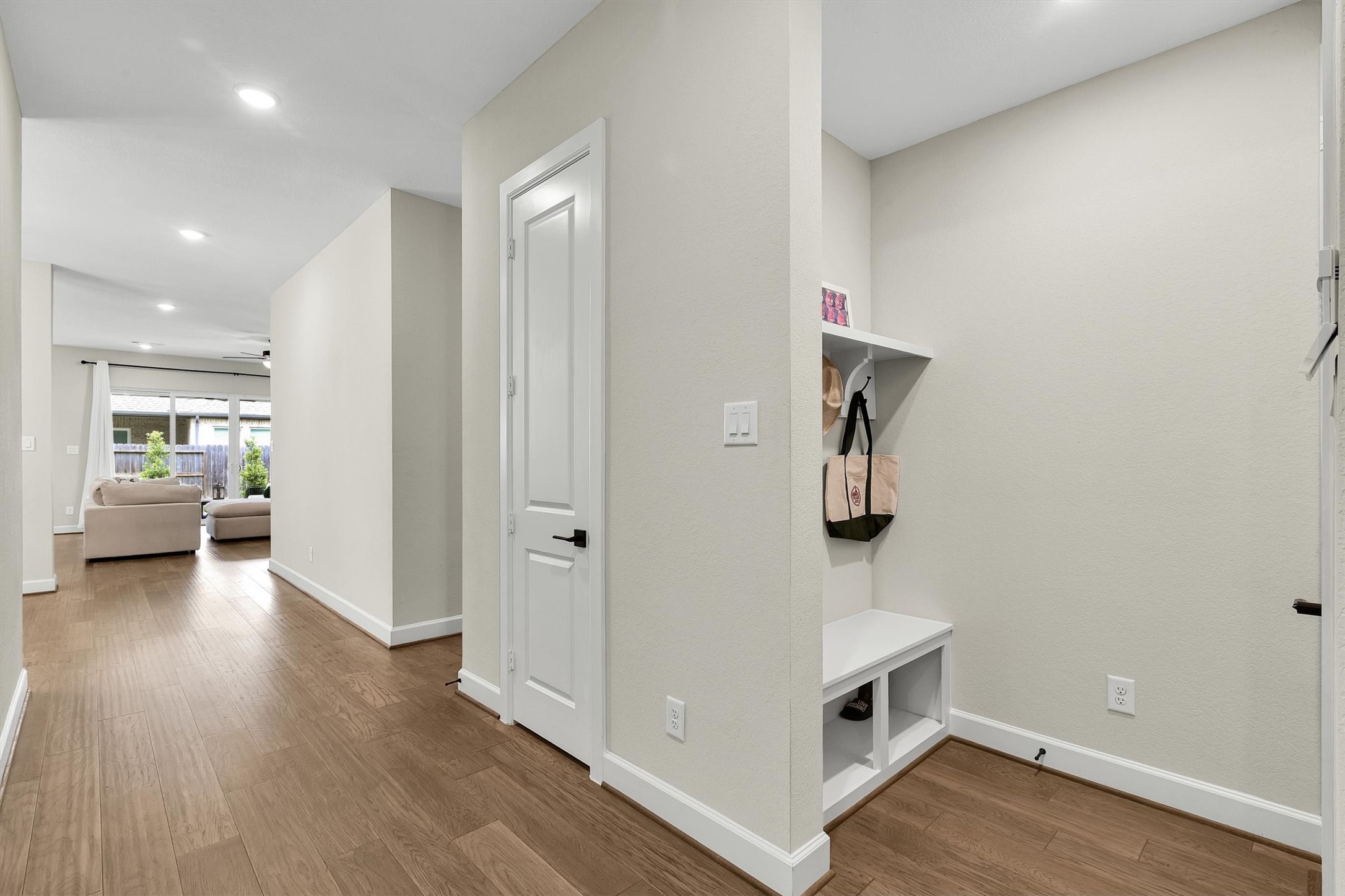 Hallway with hardwood floors leading to a bright living area. Convenient nook with hooks and storage, offering functionality and style.