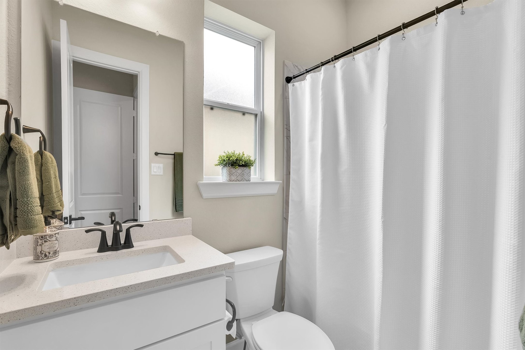 Modern bathroom featuring a sleek white vanity, a large mirror, and a tub with a white shower curtain. Plenty of natural light