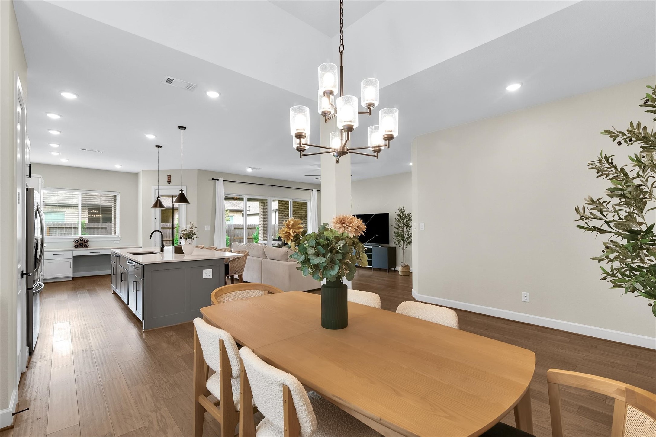 Spacious open-plan living area with a modern kitchen featuring a large island, dining area with a stylish chandelier, and a cozy living room. Bright space with ample natural light, hardwood floors, and tasteful decor, creating an inviting atmosphere.