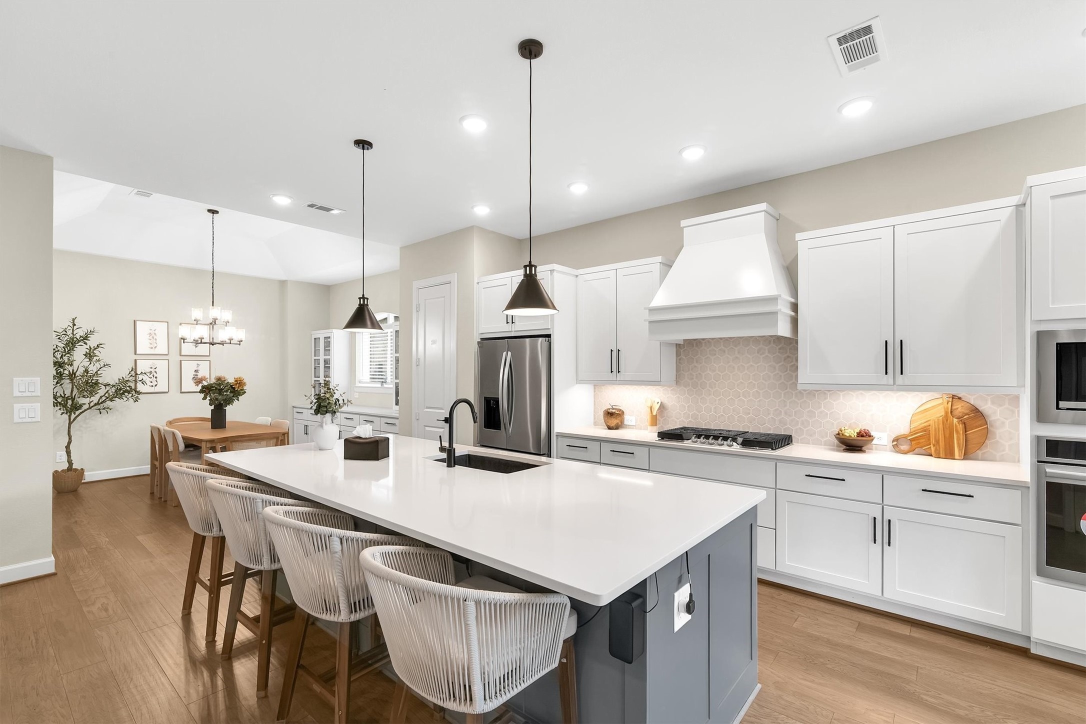 This modern kitchen features a spacious open layout with a large island, sleek white cabinetry, stainless steel appliances, and elegant pendant lighting. The adjacent dining area is bright and inviting, perfect for entertaining.