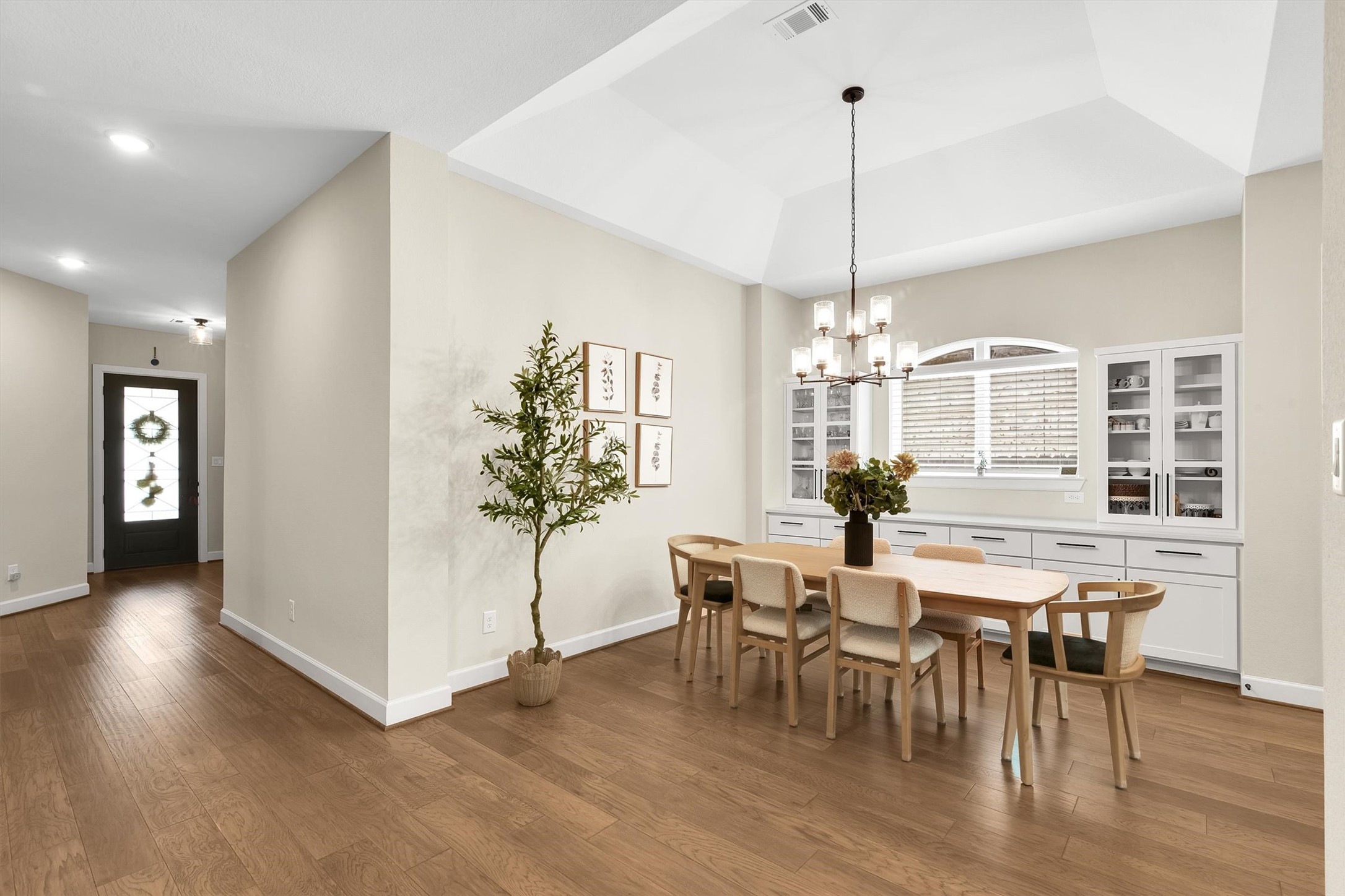 bright dining area with a contemporary chandelier, wood flooring, and a spacious built-in cabinet with glass doors. The room features a large window with an arched design, providing natural light.