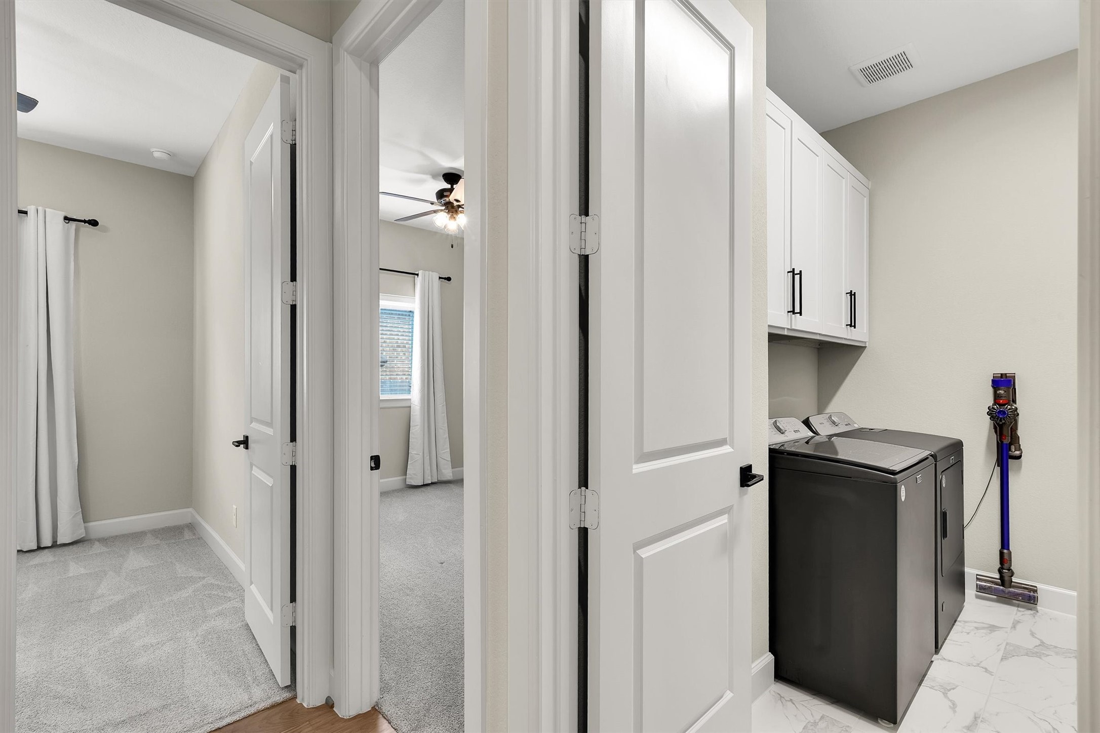 Entry to the 2nd and 3rd bedroom and laundry area. The laundry room features modern appliances, white cabinetry, and tiled floors, creating a clean and efficient space.