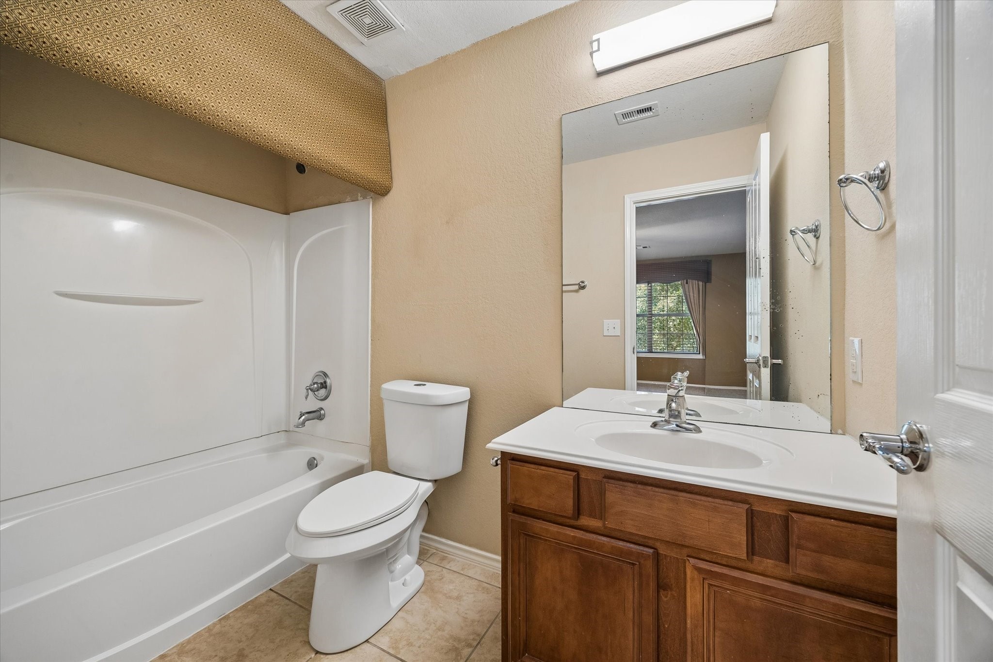 Bright full bathroom featuring a clean, white bathtub, sleek vanity with ample storage, and a large mirror, complemented by neutral tones and warm tile flooring.