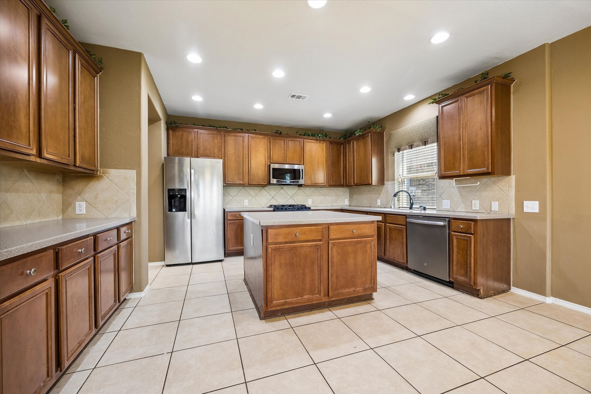 Spacious kitchen with warm wood cabinetry, a central island, stainless steel appliances, and ample counter space for meal preparation and entertainment.