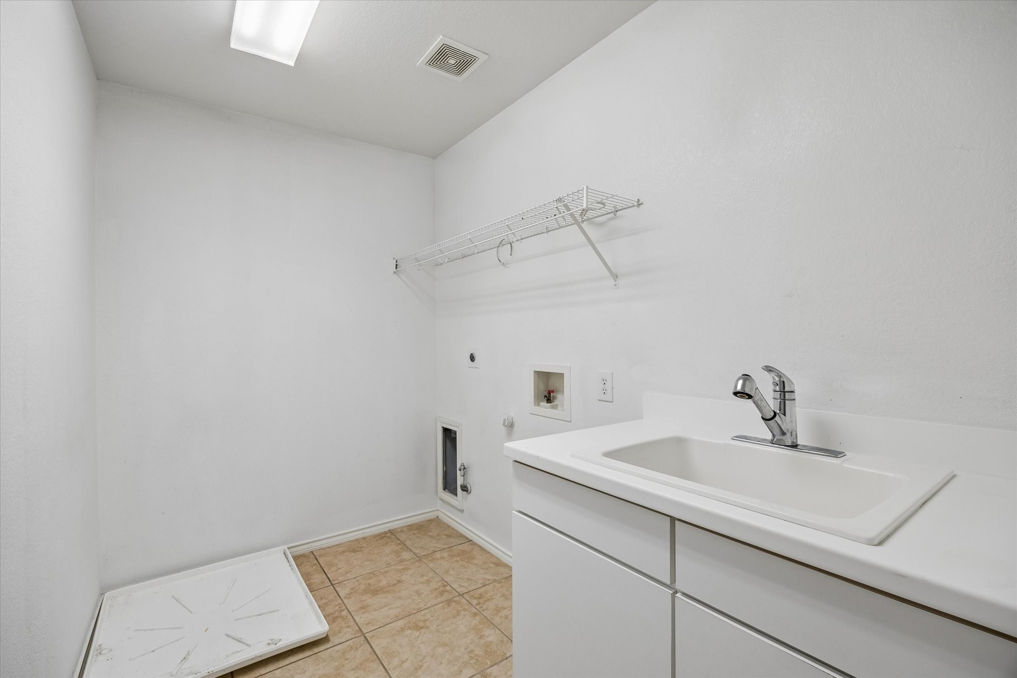 Spacious laundry room with a utility sink, built-in shelving, and tiled flooring, ready for your washer and dryer setup.