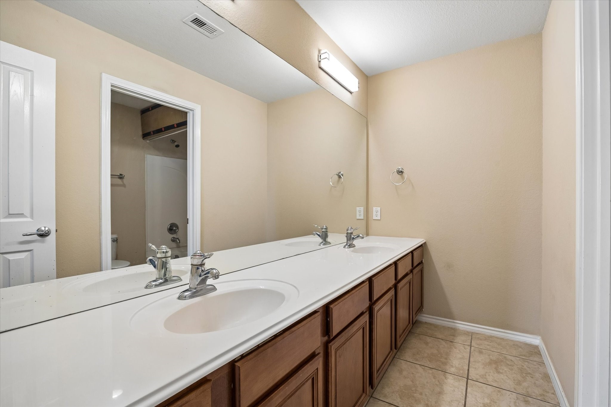 Spacious bathroom featuring a double sink vanity with elegant fixtures, ample cabinet storage, and a large mirror enhancing the light and space.