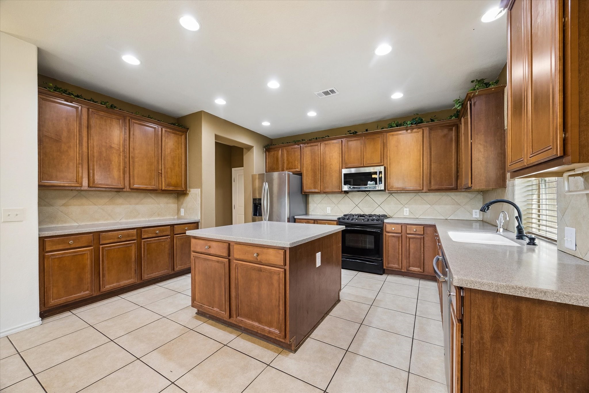 Spacious kitchen featuring rich wood cabinetry, a central island, modern stainless steel appliances, and ample counter space, perfect for culinary enthusiasts.