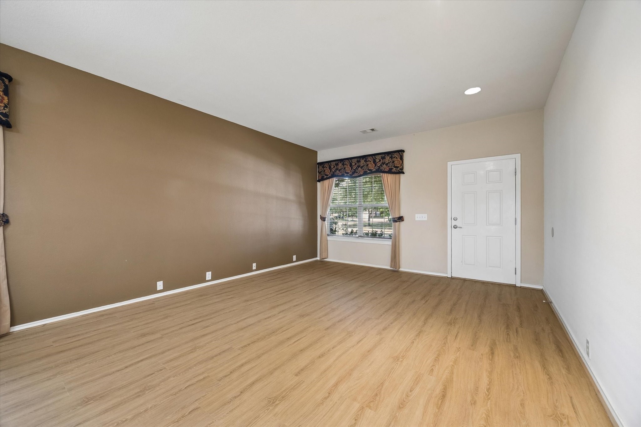 Spacious room with warm wood flooring, neutral walls, and a large window providing ample natural light.