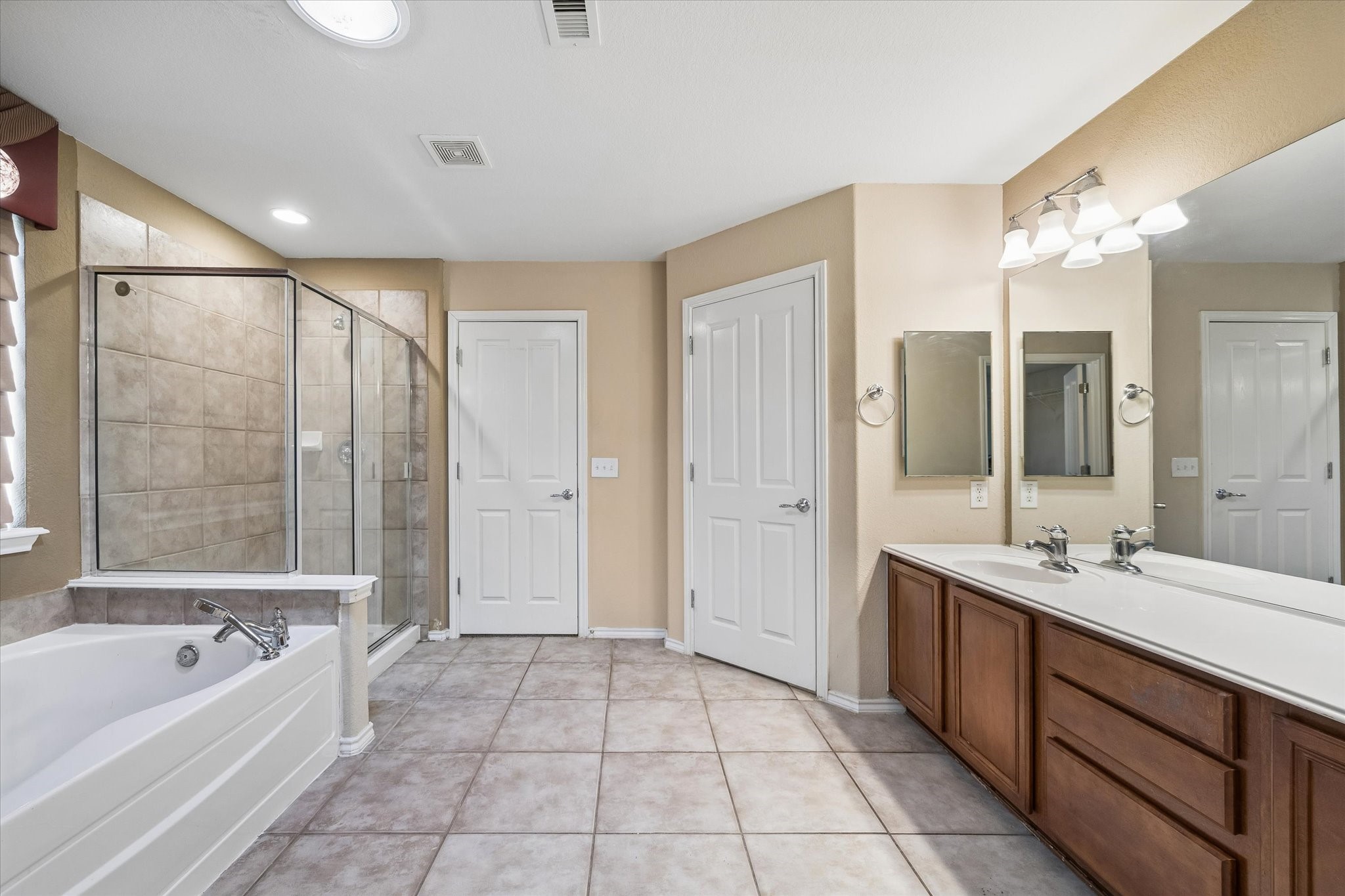 Spacious primary bathroom featuring a large walk-in shower, relaxing soaking tub, dual sinks with ample counter space, and elegant tile flooring.