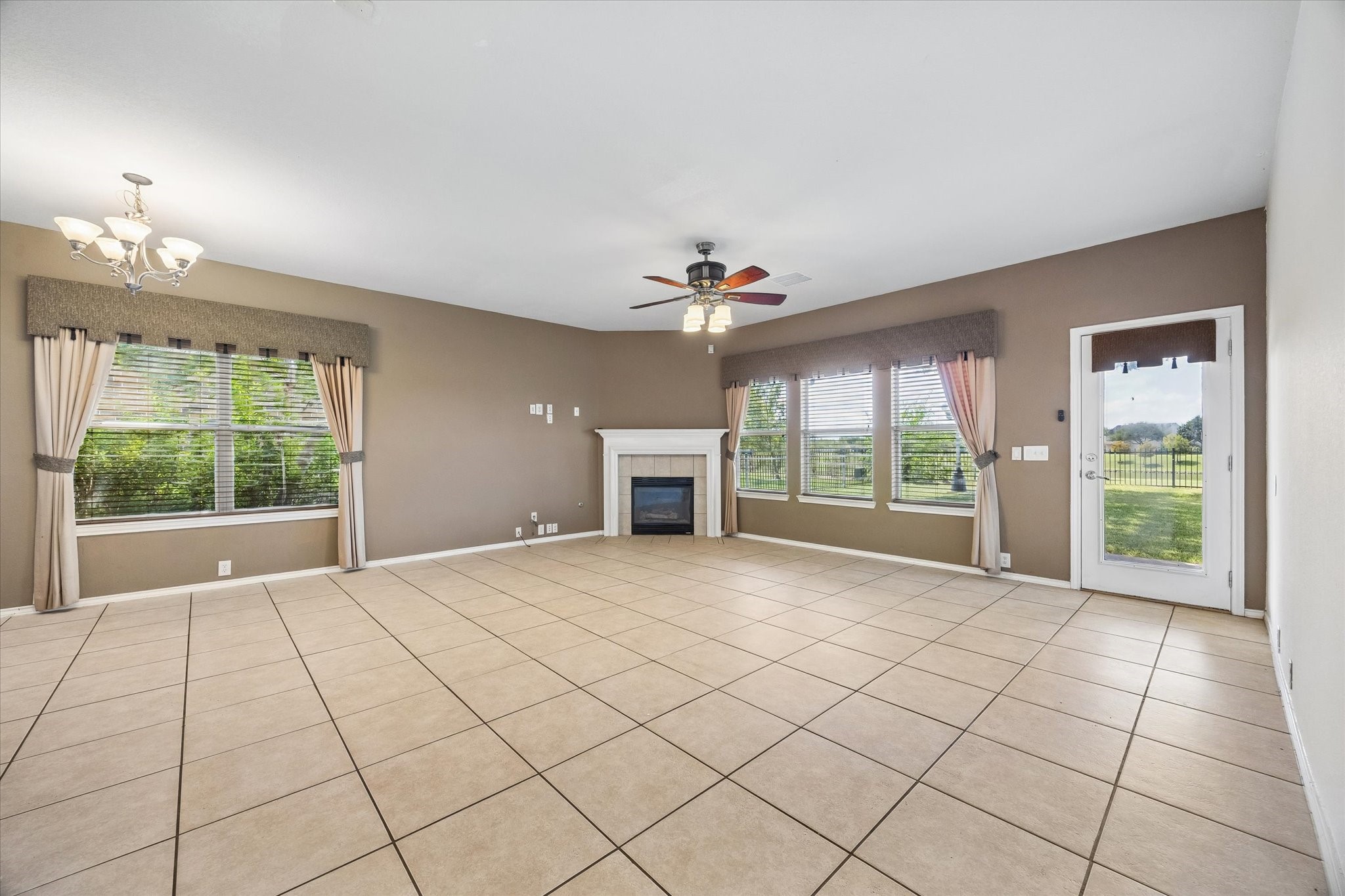 Spacious family room with large windows offering natural light, a cozy fireplace, elegant tile flooring, and direct access to a scenic water-view backyard.