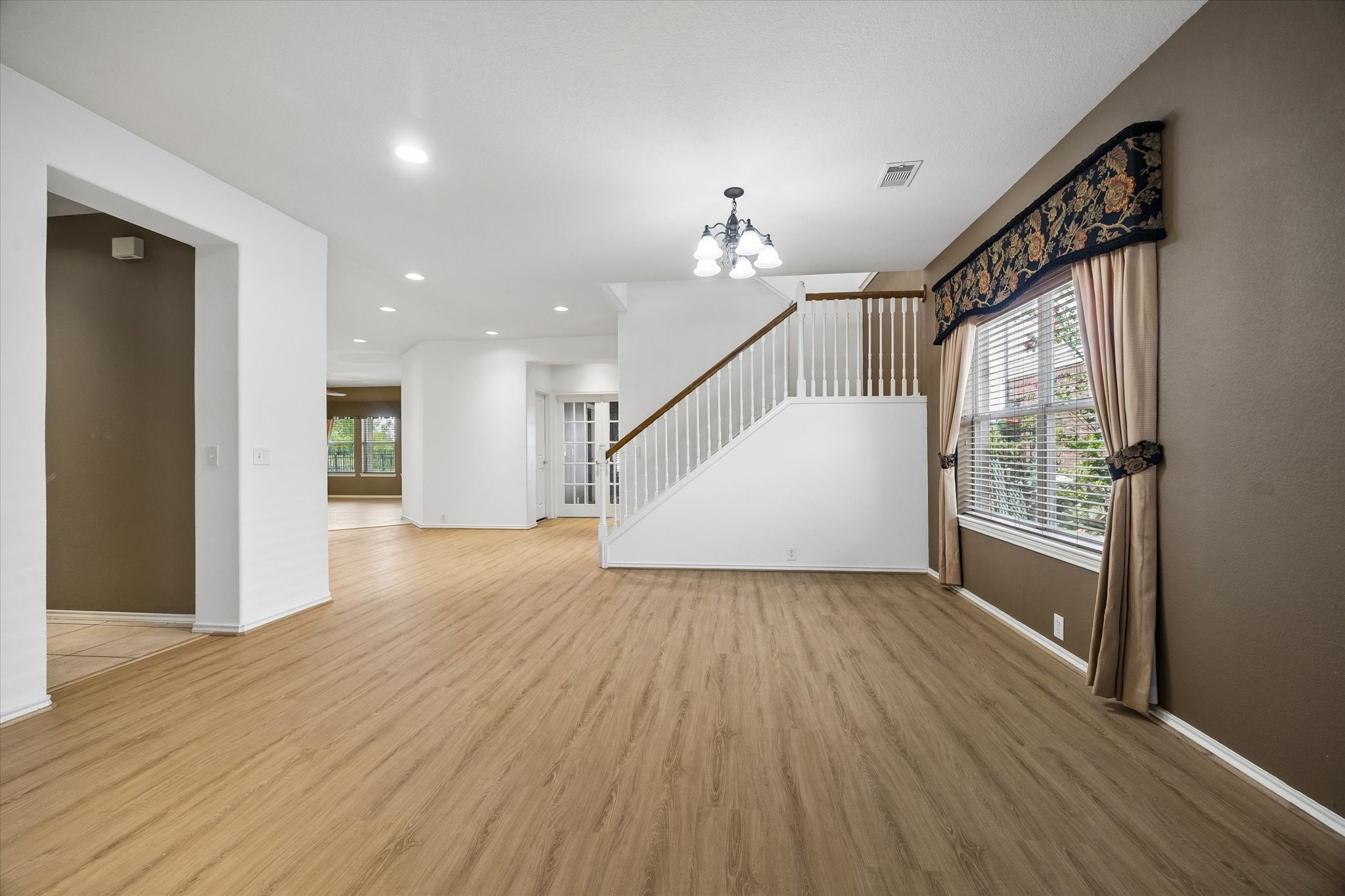 Spacious living area with elegant wood flooring, featuring a stylish staircase, large windows, and modern light fixtures.
