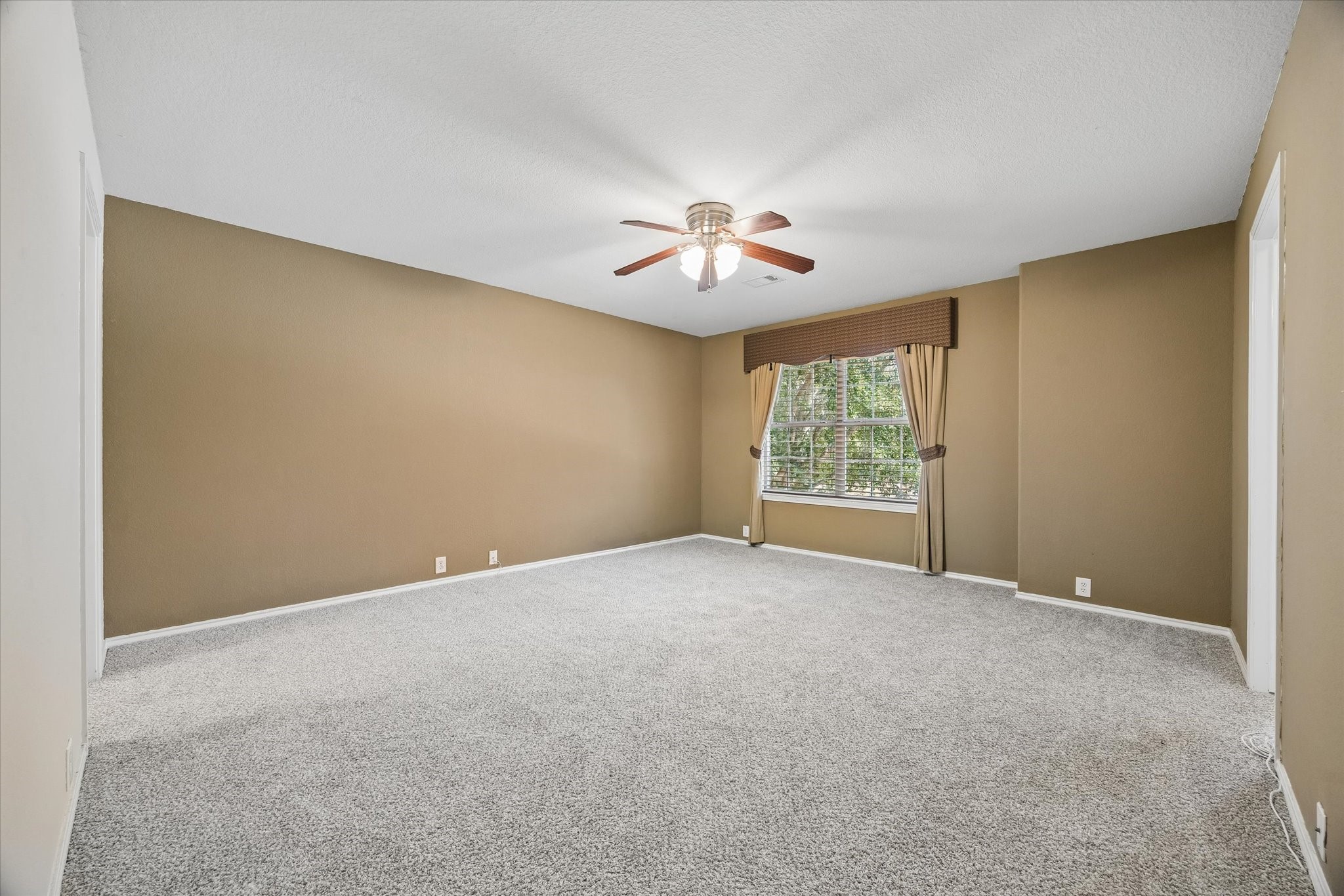 Spacious secondary bedroom with warm neutral walls, plush carpeting, and a ceiling fan, complemented by a large window.