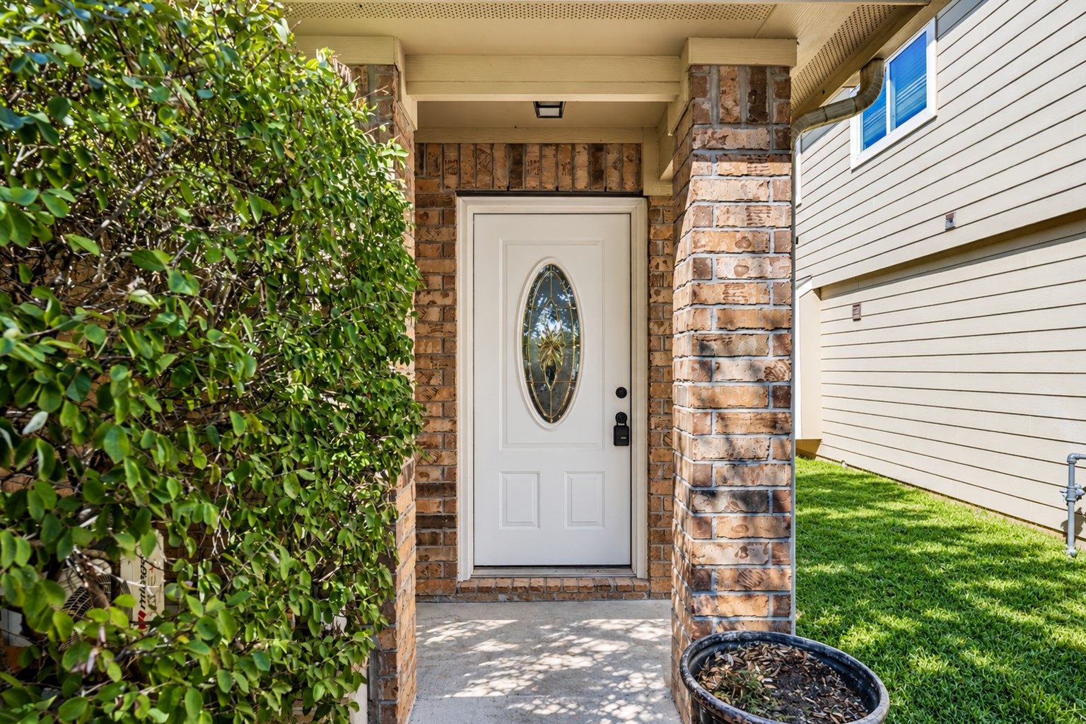 Welcoming front entryway featuring a classic brick column, mature landscaping, and a secure front door with a decorative glass insert. Welcoming front entryway featuring a classic brick column, mature landscaping, and a secure front door with a decorative glass insert.