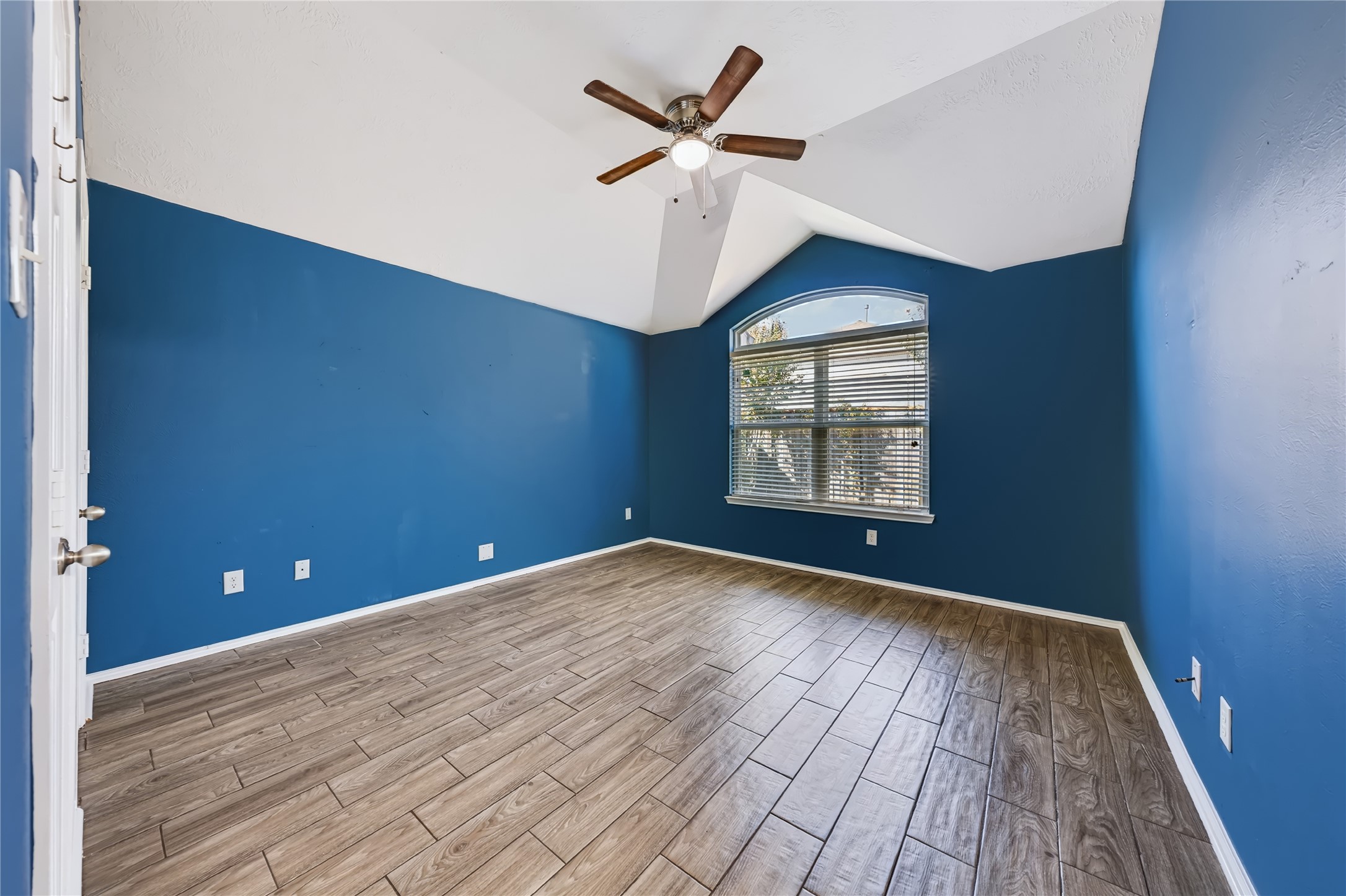 Spacious master bedroom featuring high vaulted ceilings, rich wood-look tile flooring, an upgraded ceiling fan, and large windows bringing in plenty of natural light.