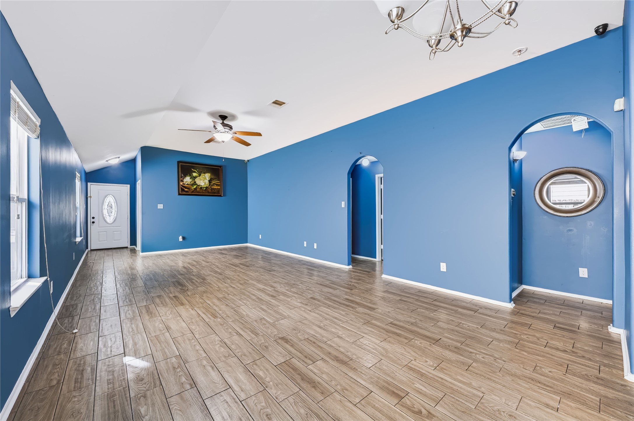 Spacious open-concept living area featuring rich wood-look tile flooring, vaulted ceilings, a modern ceiling fan, and vibrant accent walls. Spacious open-concept living area featuring rich wood-look tile flooring, vaulted ceilings, a modern ceiling fan, and vibrant accent walls.